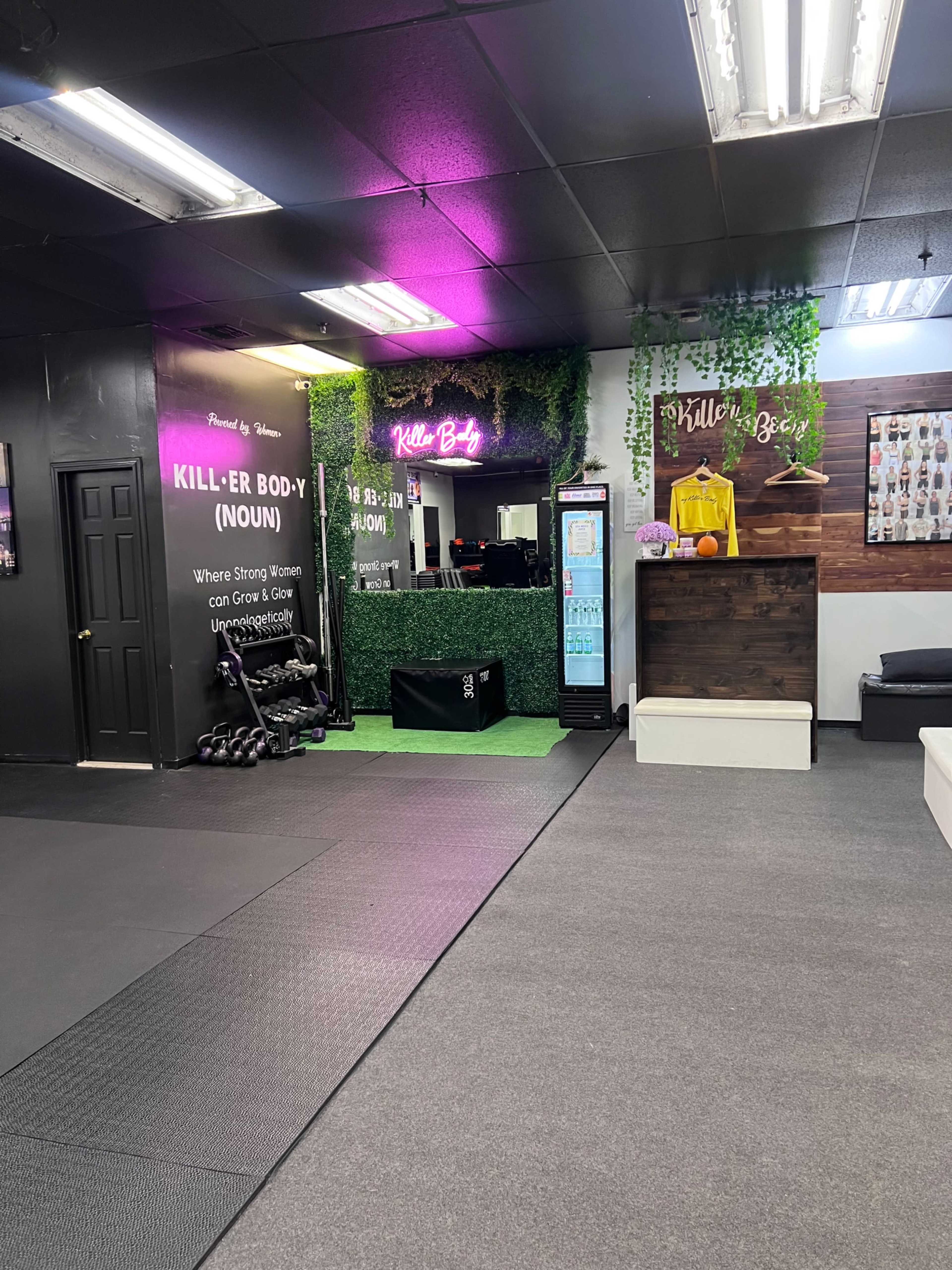The image shows a fitness studio entrance with a sign reading "KILL-ER BODY" and workout equipment visible in the background.