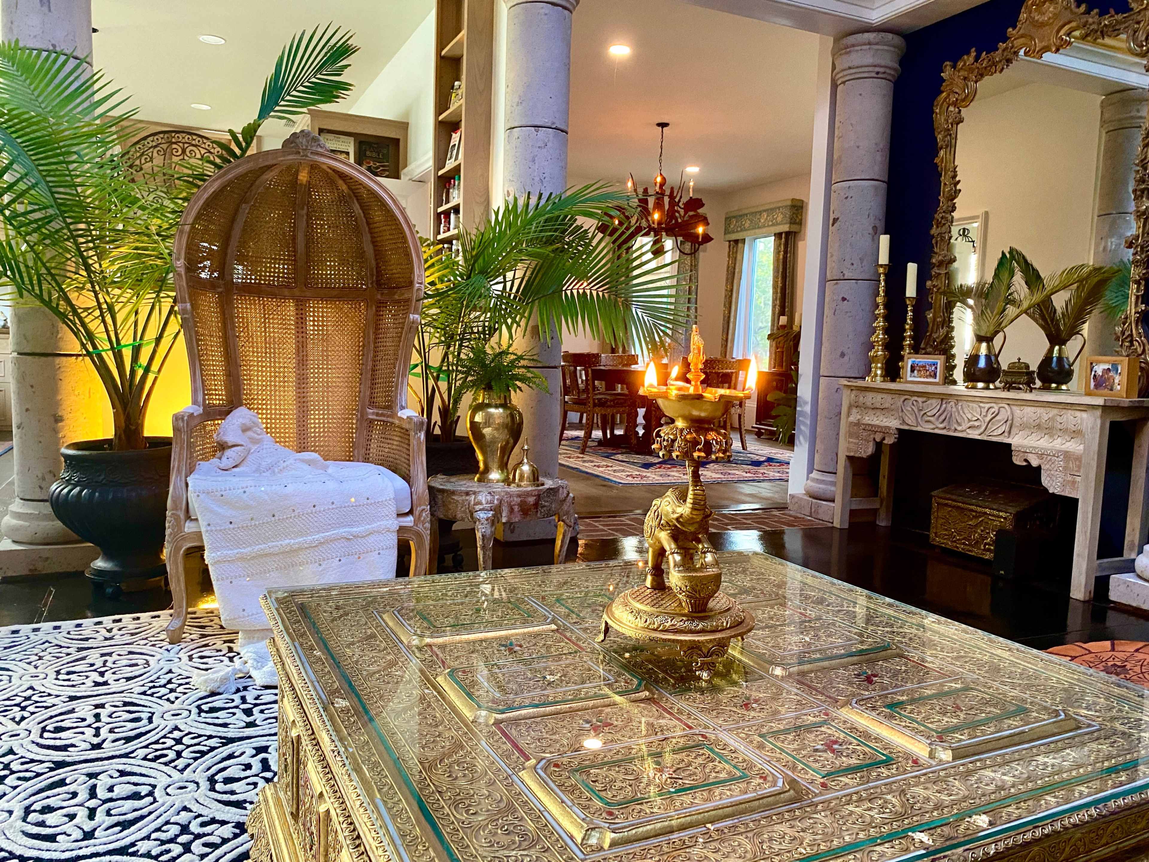 A beautifully decorated living room featuring a large ornate chair, a glass-topped coffee table, and intricate decor elements like plants and sculptures.