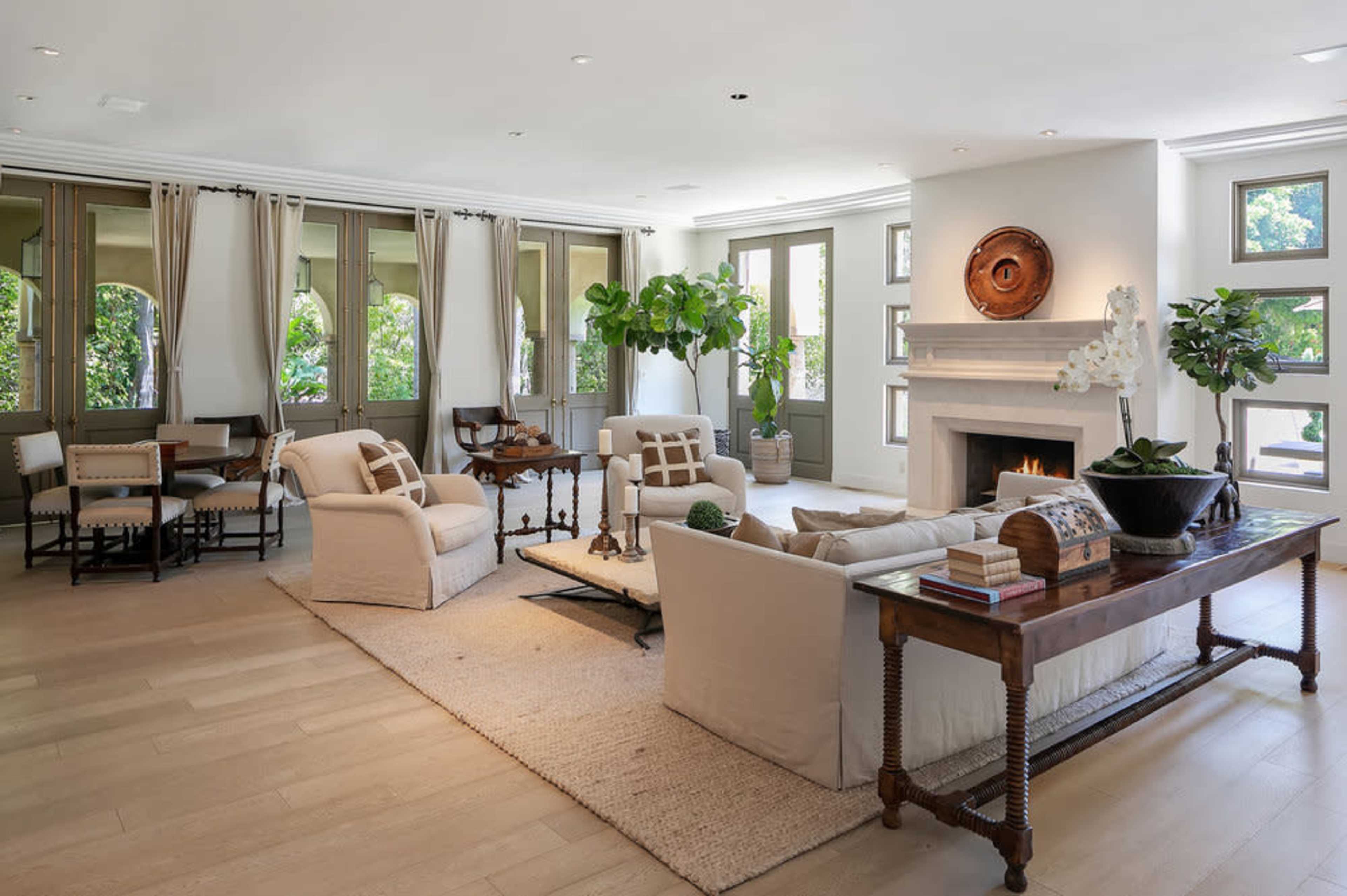 The image shows a modern living room with beige furniture, a wooden table, and large windows allowing natural light.