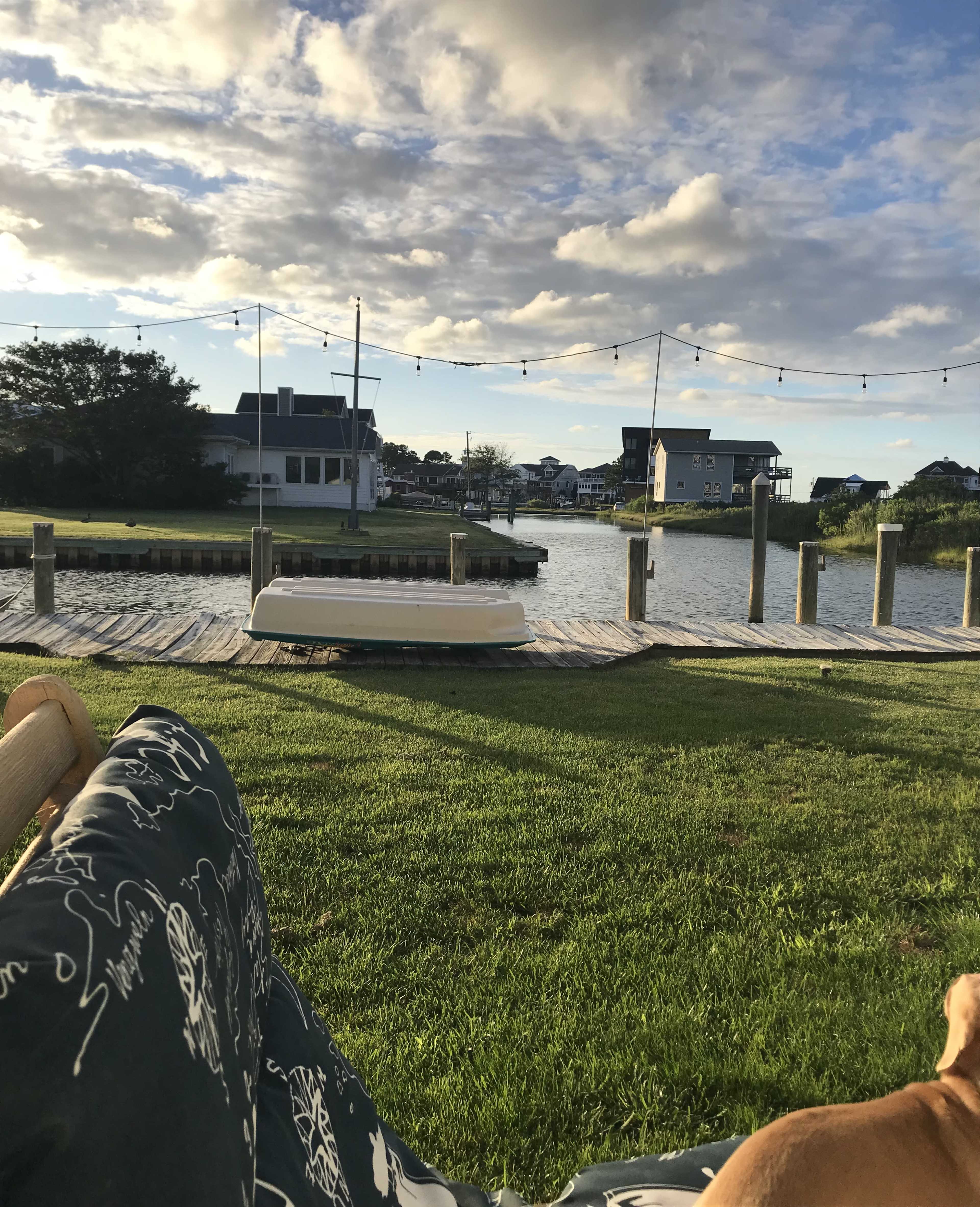 A boat dock on a calm waterway with several houses in the background and clouds in the sky.