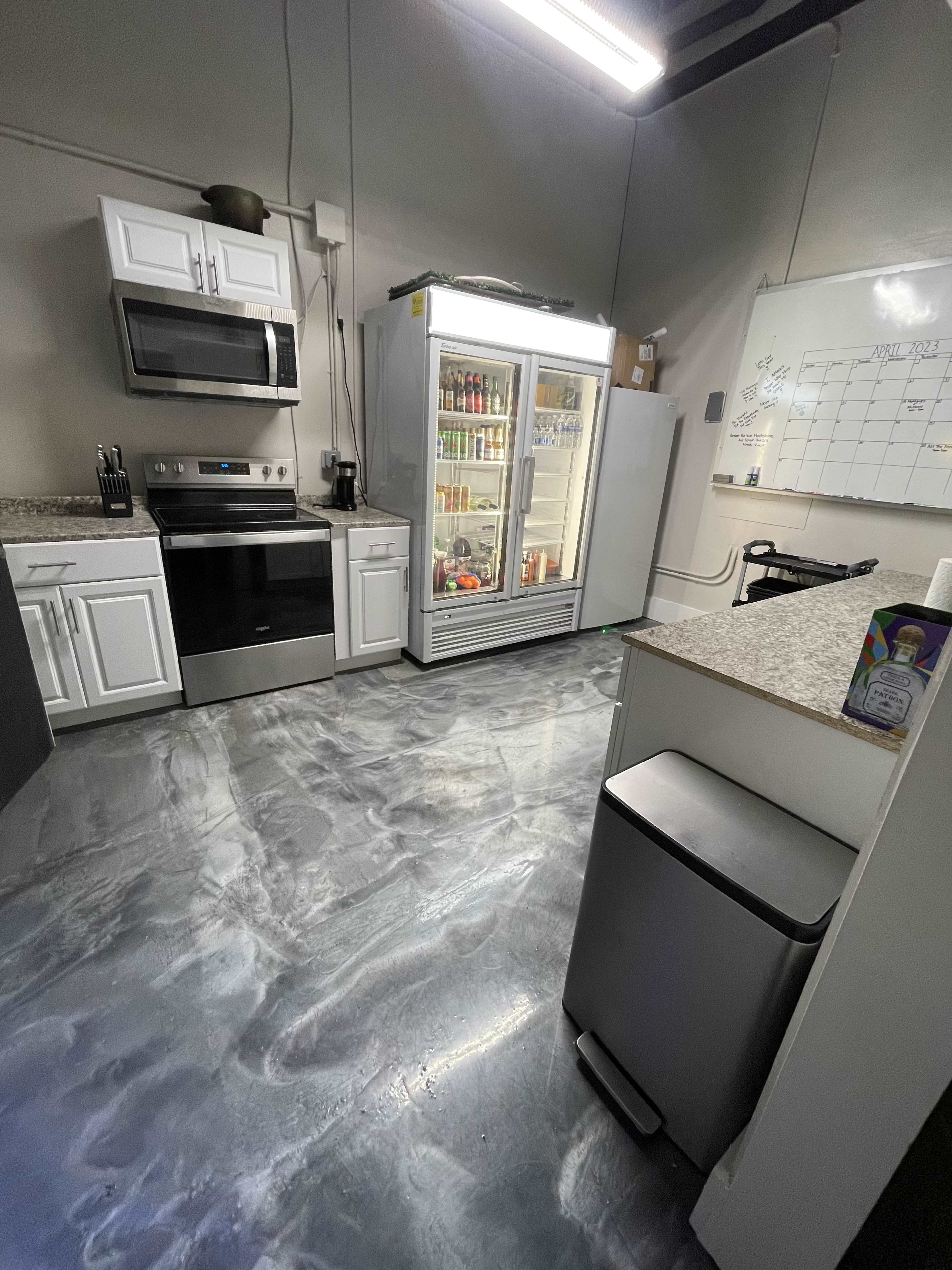 The image shows a modern kitchen with white cabinets, a stainless steel stove, a refrigerator filled with drinks, and a gray polished floor.