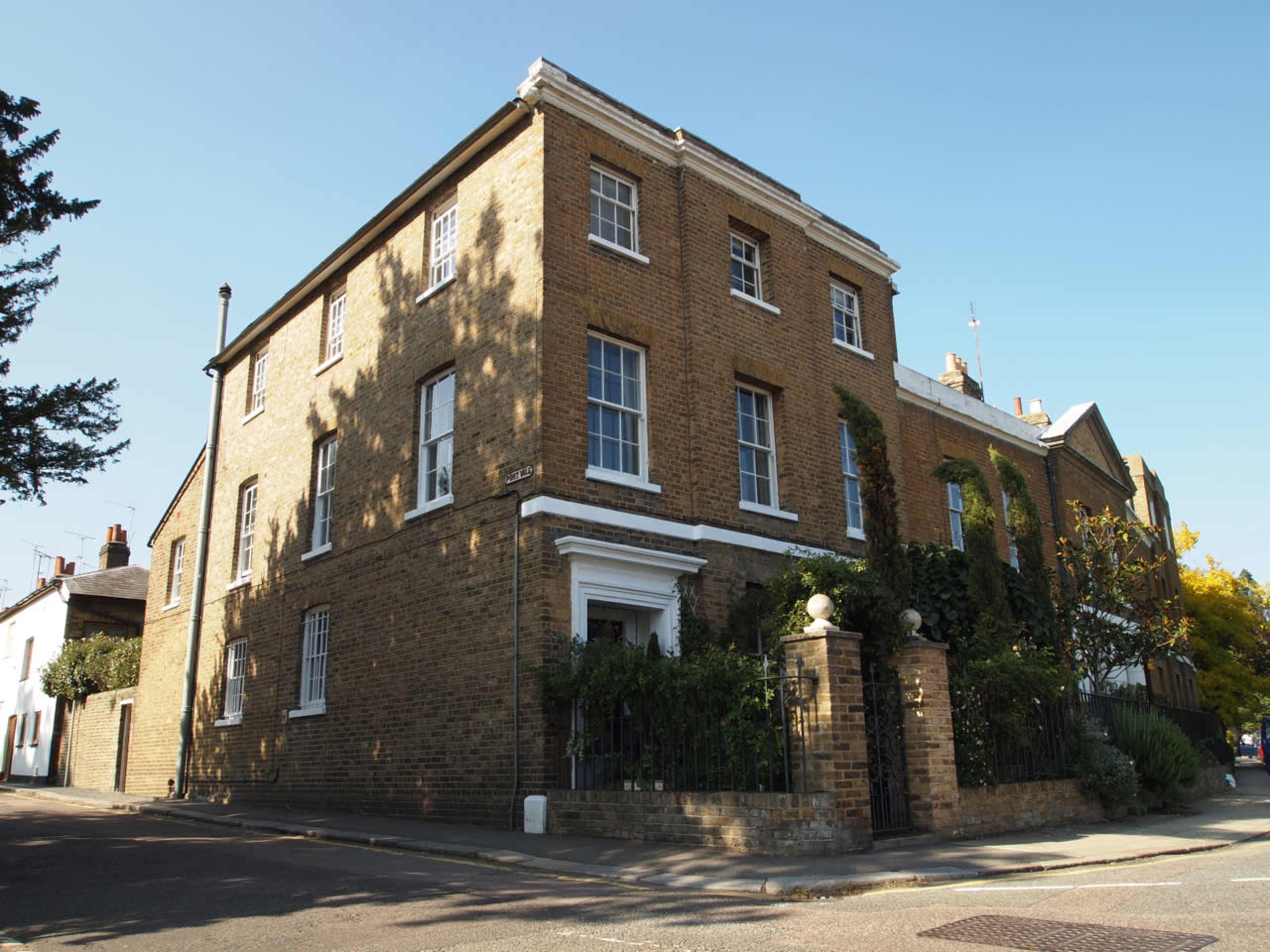 The image shows a two-story brick house with white trim and a small garden, located at the intersection of two streets.