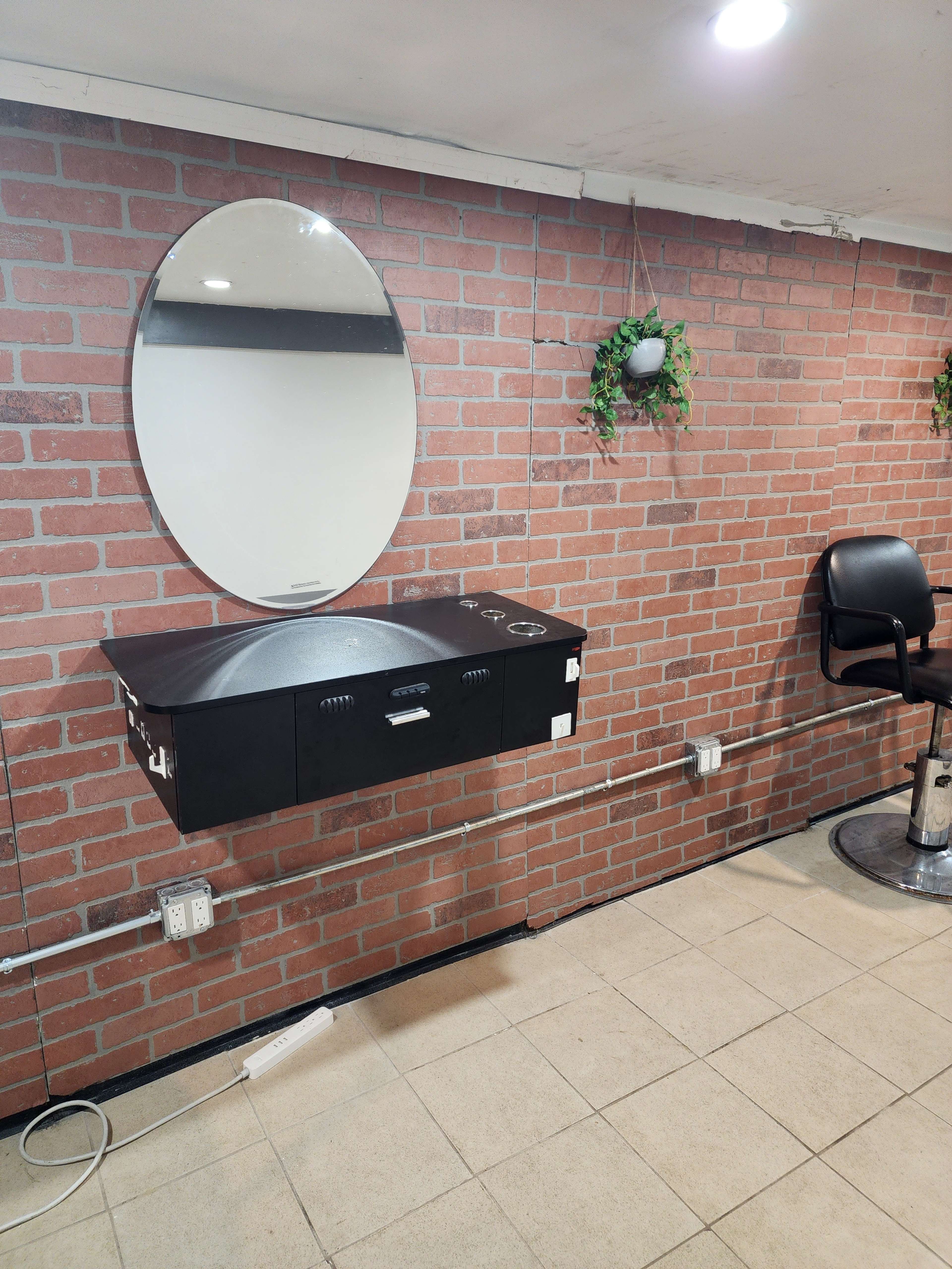 A wall-mounted black vanity with a circular mirror above it, set against a red brick wall in a room with tiled flooring.