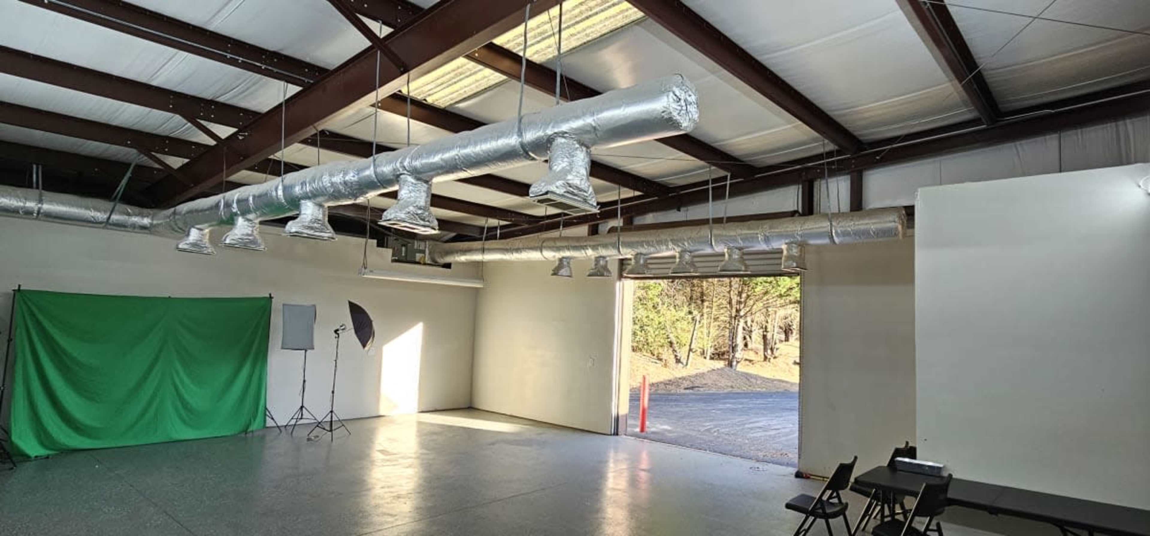 An empty industrial-style room with metal beams, ventilation ducts, and a green backdrop set against a wall.