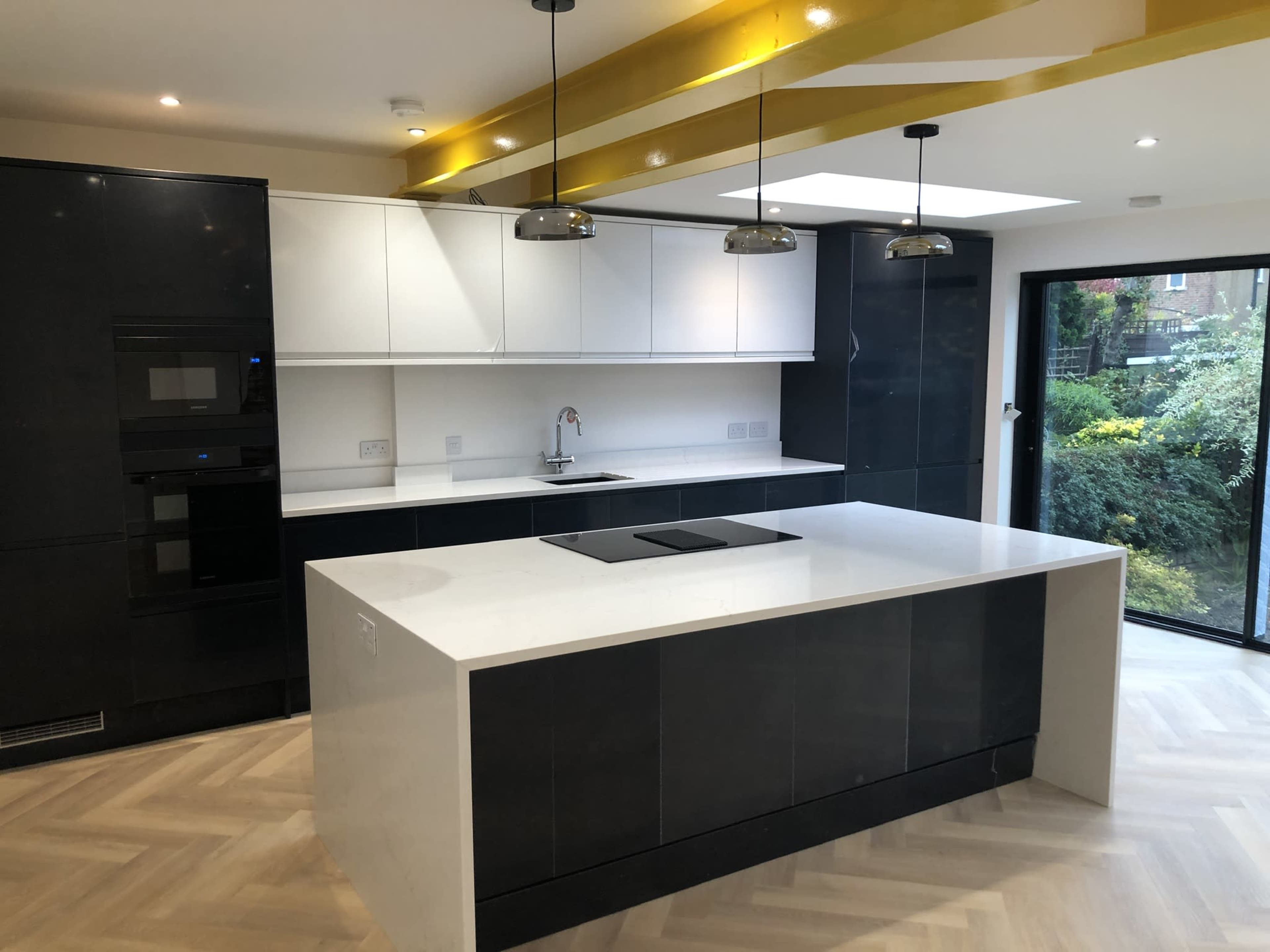 The image shows a modern kitchen with a central island, sleek black and white cabinetry, and gold accents on the ceiling.