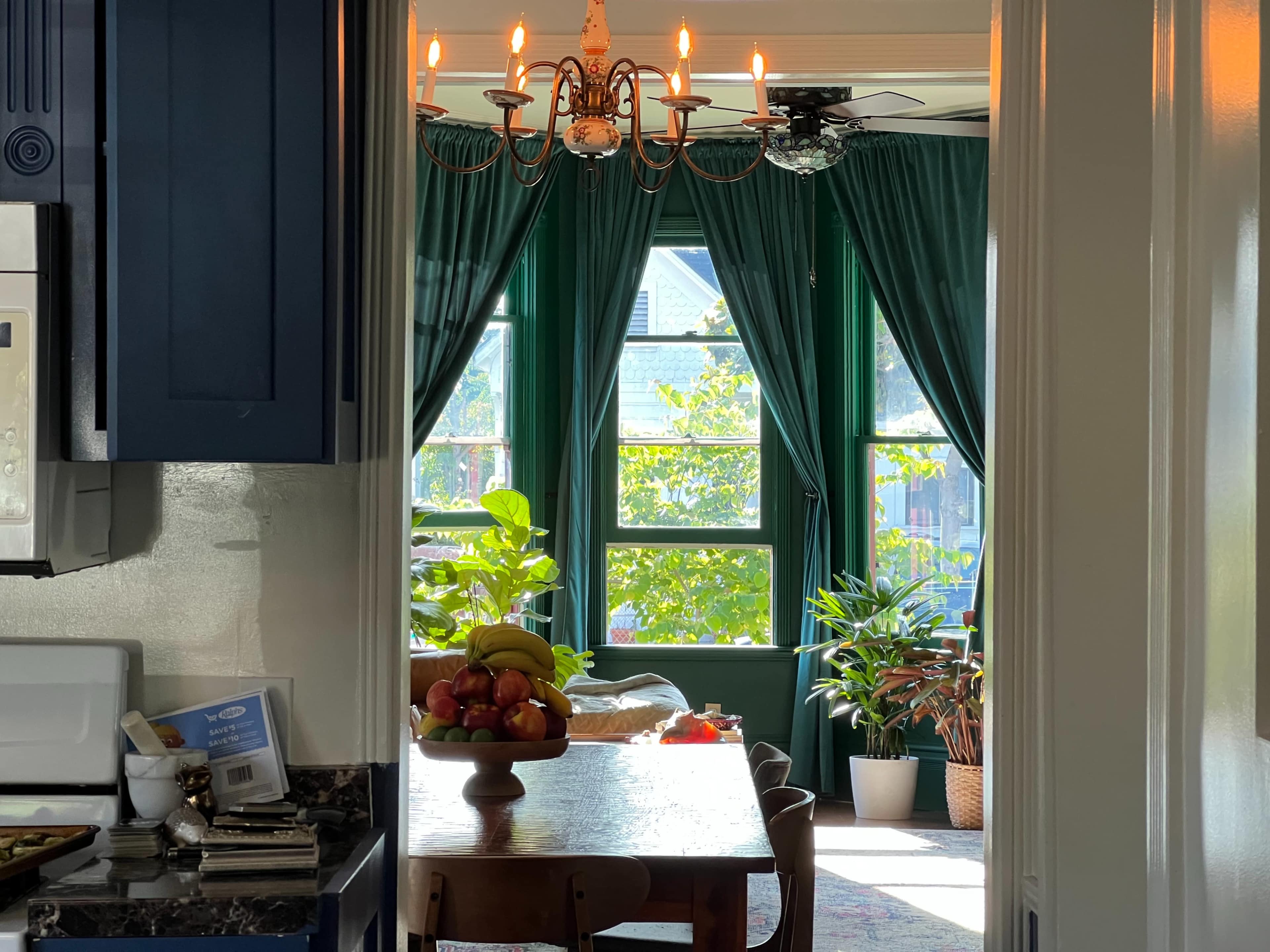 A kitchen with a view through an open doorway into a sunlit room filled with plants and a dining table.
