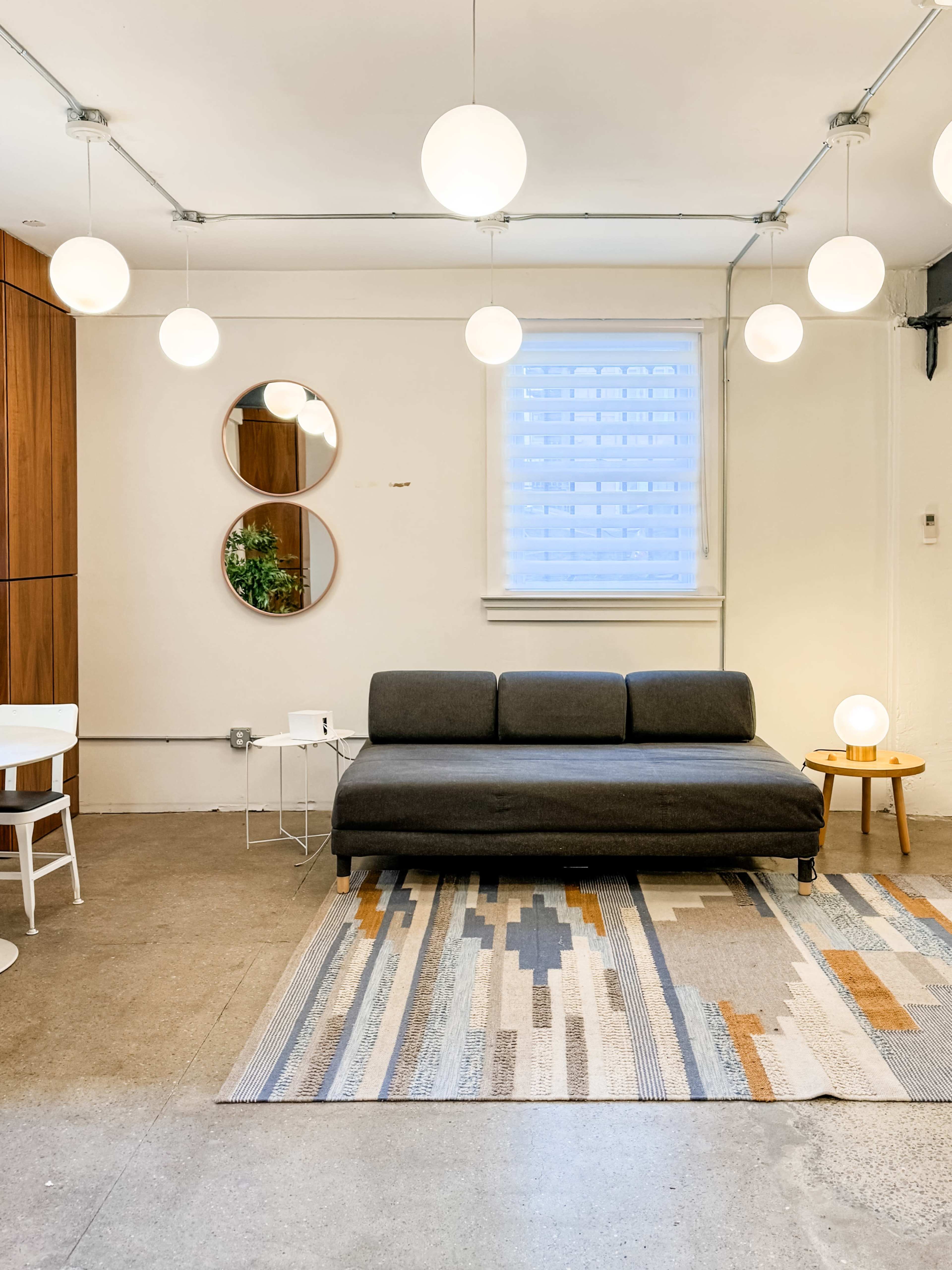 A modern living space with a gray sofa, round mirror, and several spherical pendant lights hanging from the ceiling.