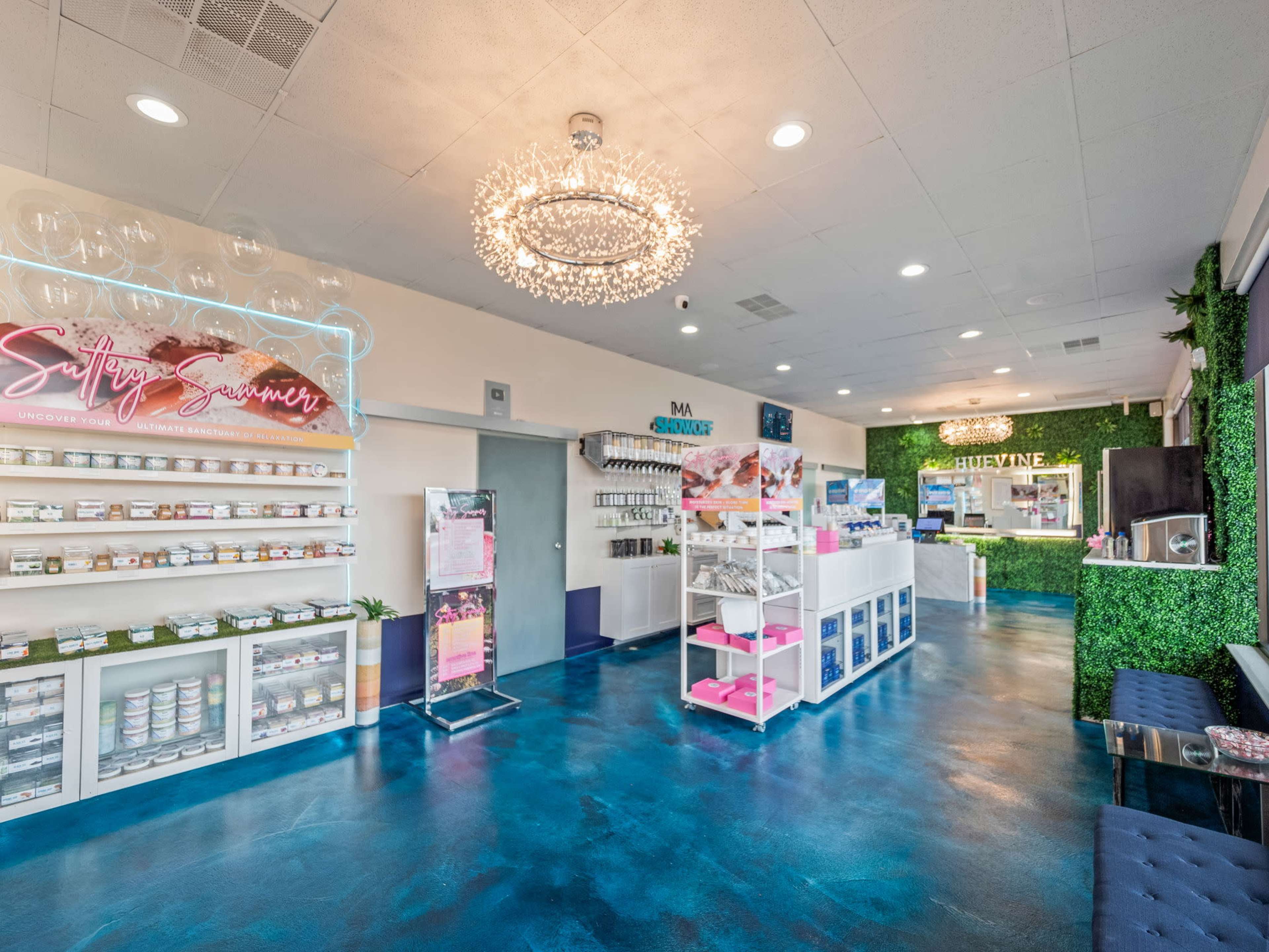 A brightly lit spa interior with a modern design featuring shelves of products, a reception desk, and greenery accents on the walls.