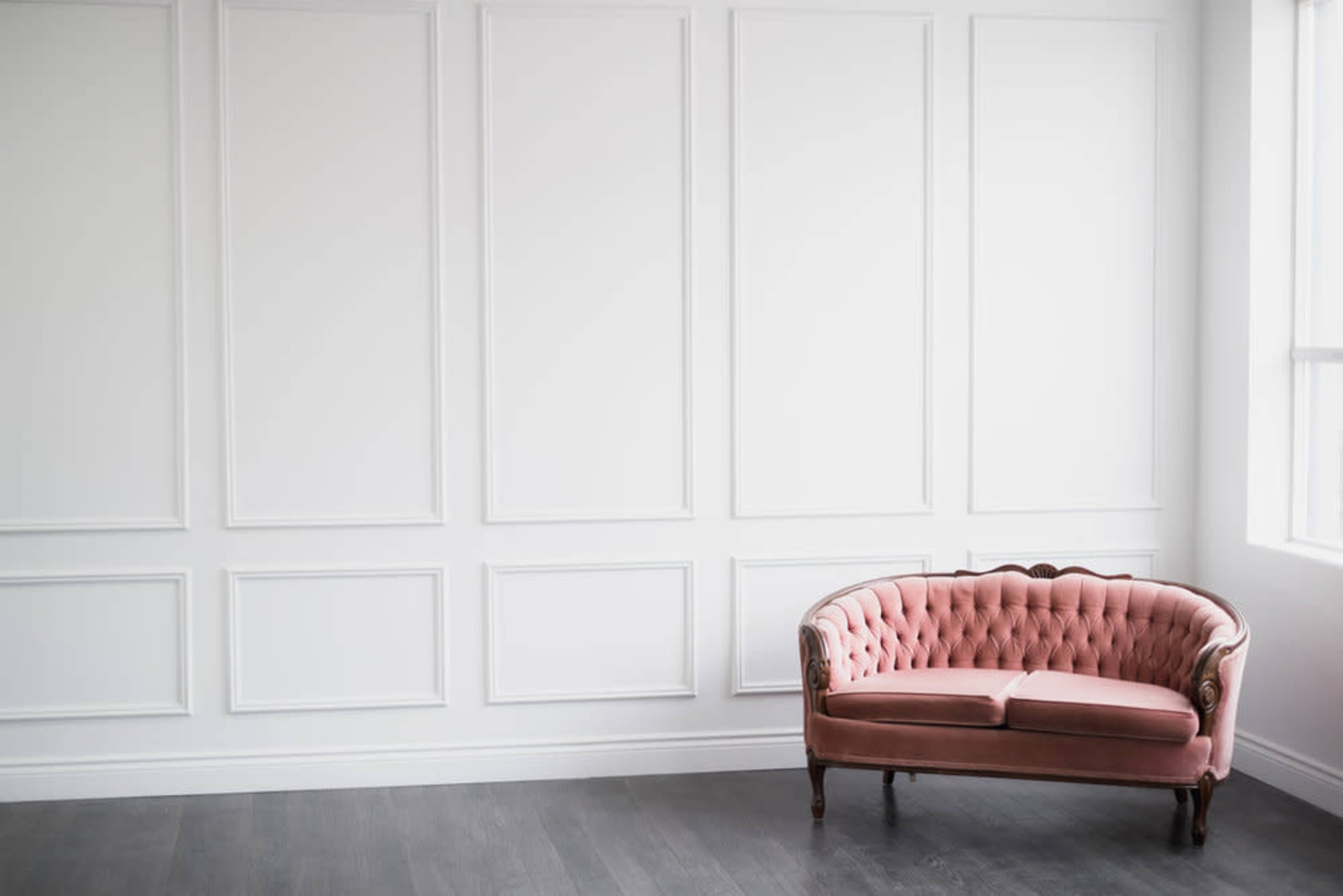 A tufted pink sofa is positioned against a white paneled wall in a brightly lit room.