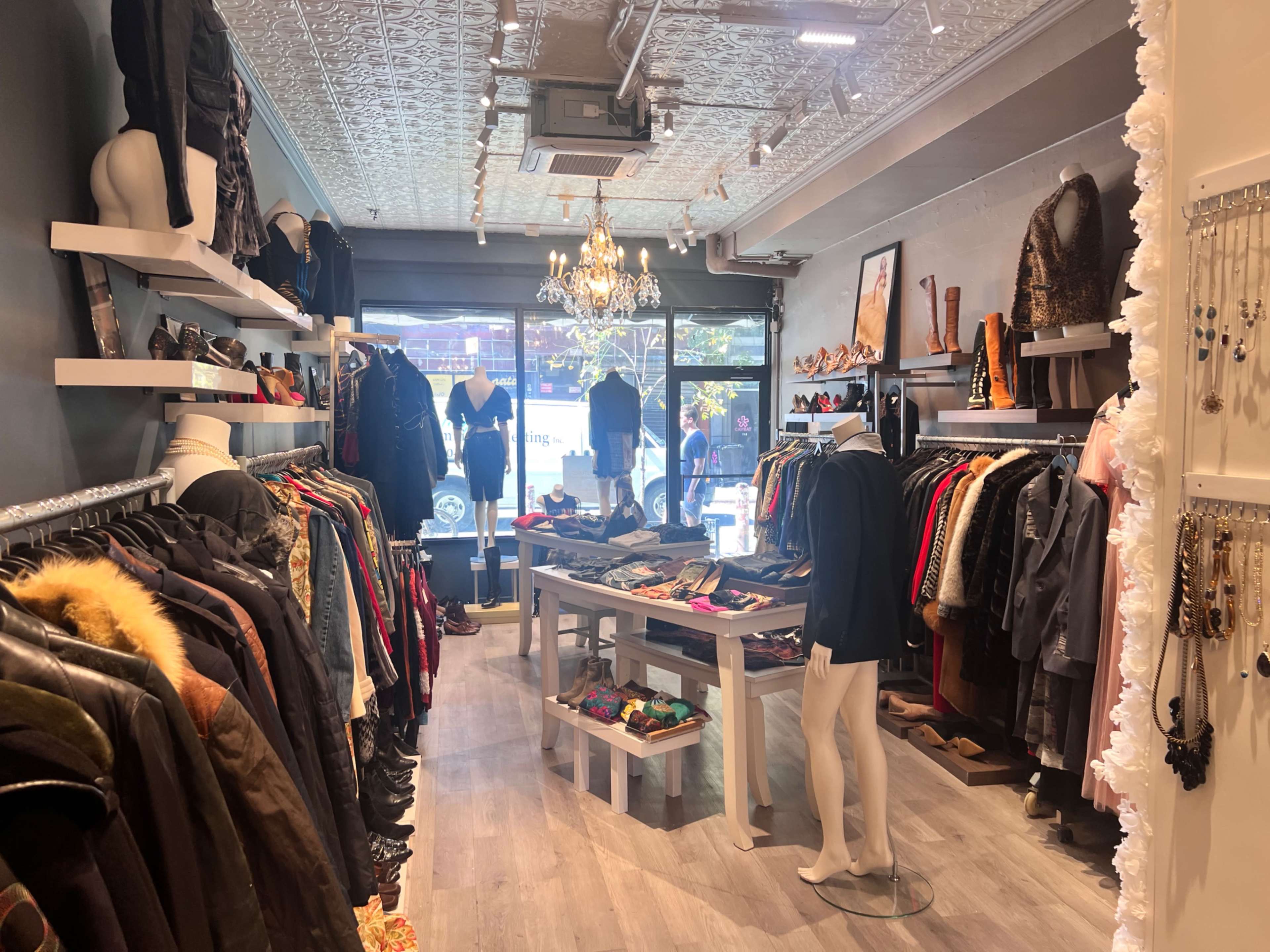 The image shows a clothing boutique featuring rows of apparel on racks, display tables with accessories, and large windows allowing natural light to enter.