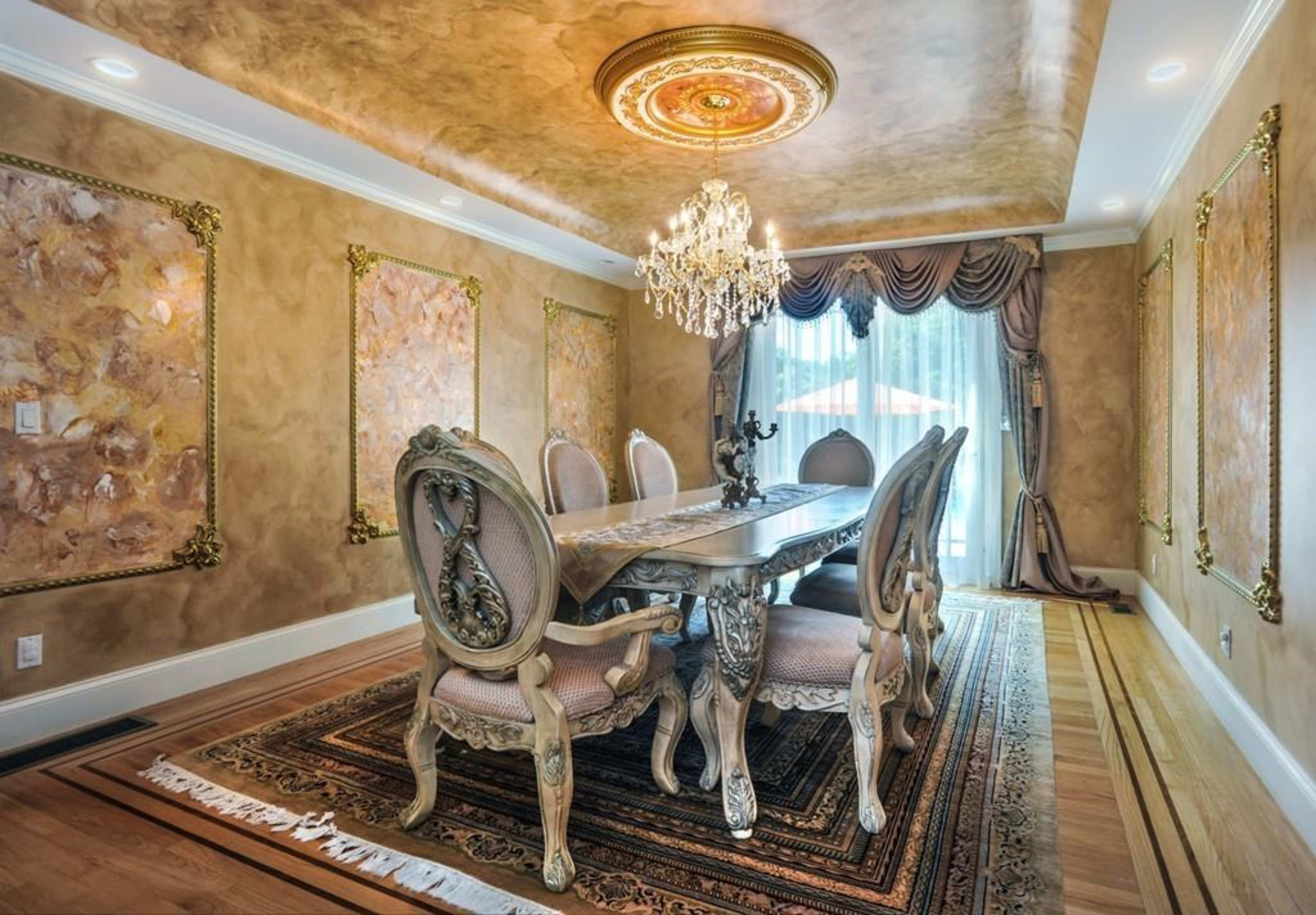 The image shows an elegantly designed dining room featuring a large table surrounded by ornate chairs, a sparkling chandelier, and decorative wall panels.