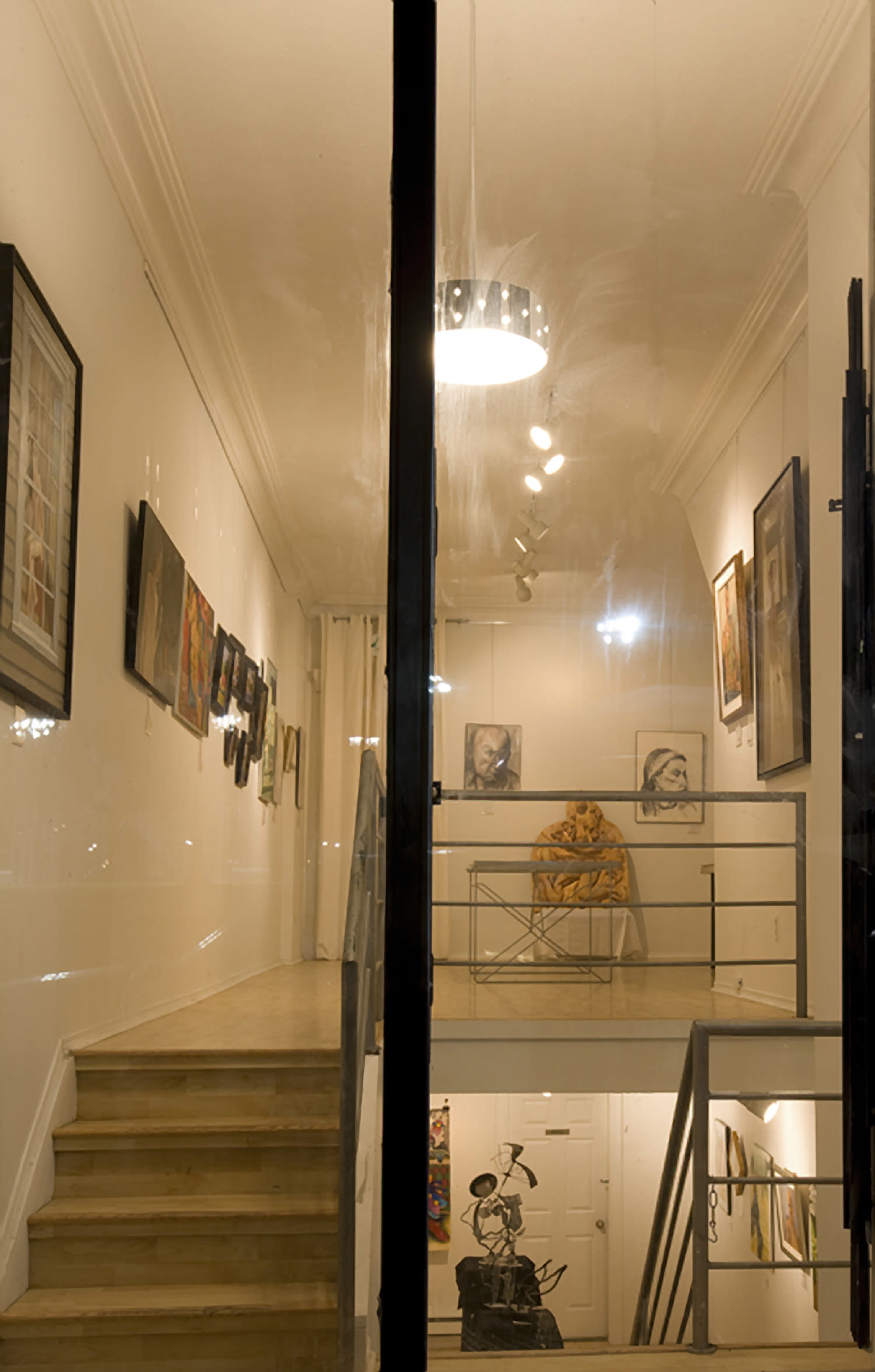 An art gallery with a staircase leading to an upper level, featuring framed artworks on the walls and a sculpture visible on the lower floor.