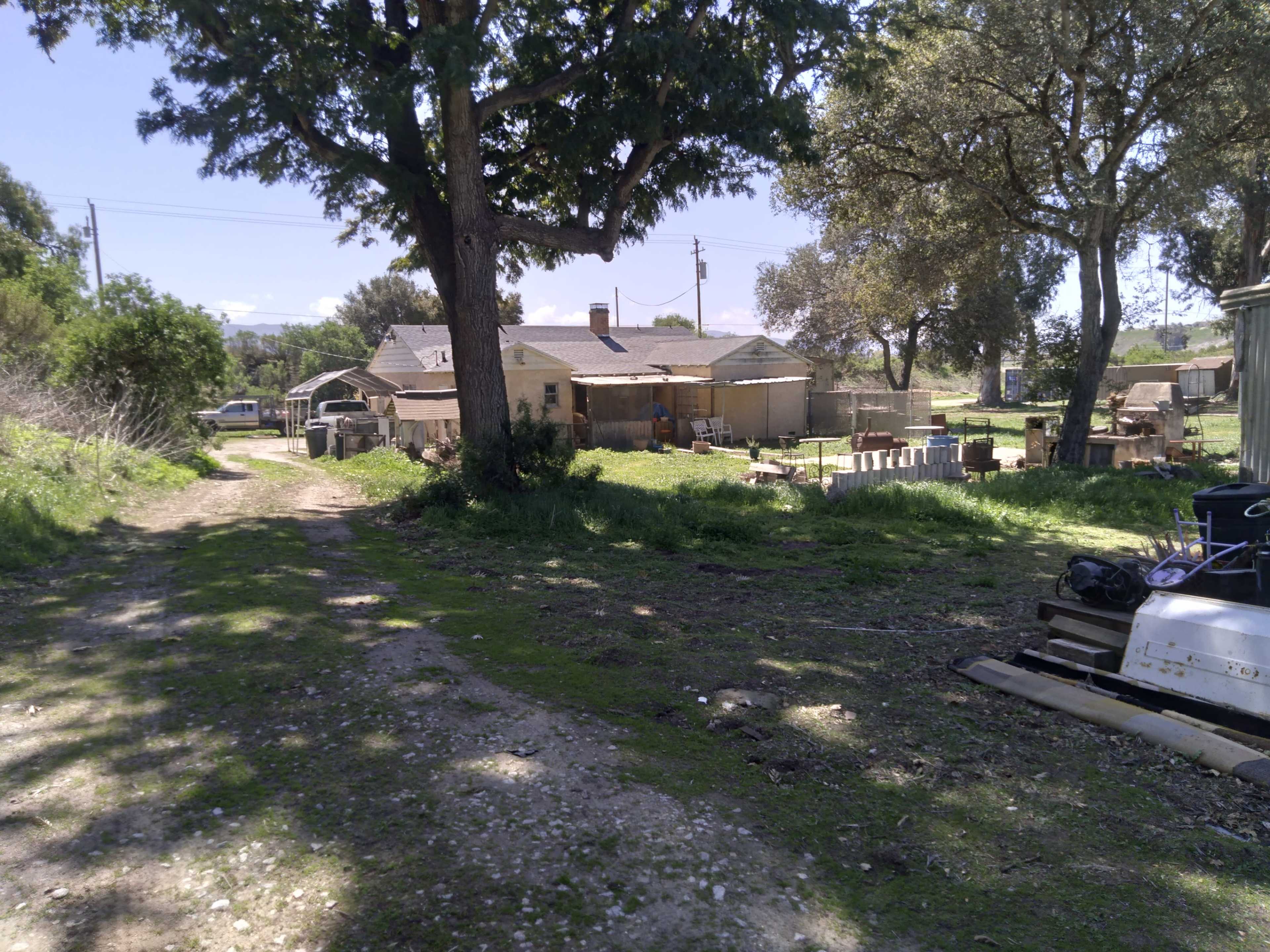 A dirt path leads towards a cluster of buildings surrounded by trees and open land.