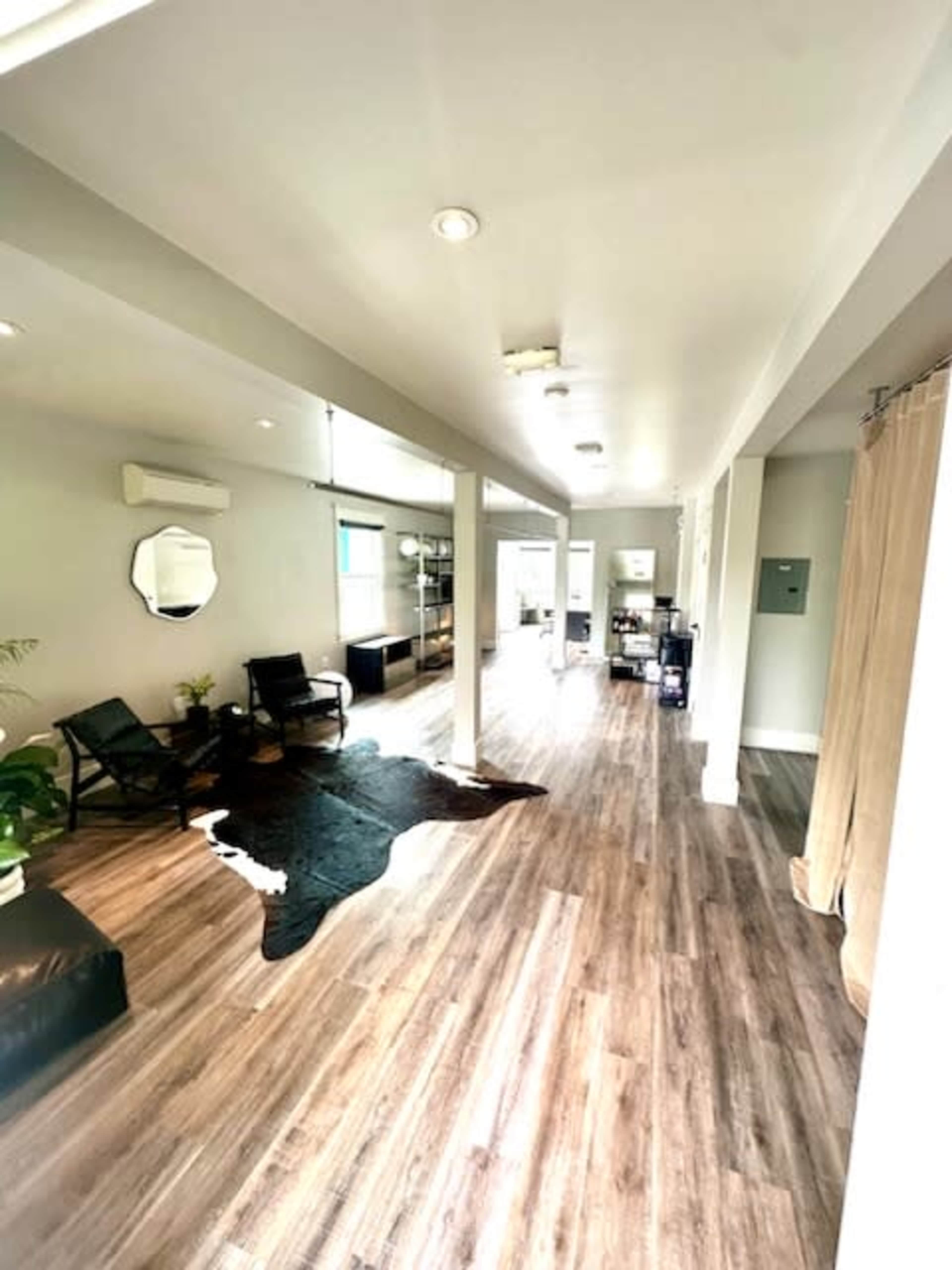 A spacious, modern interior with wooden flooring, two black chairs, a large cowhide rug, and bright lighting.