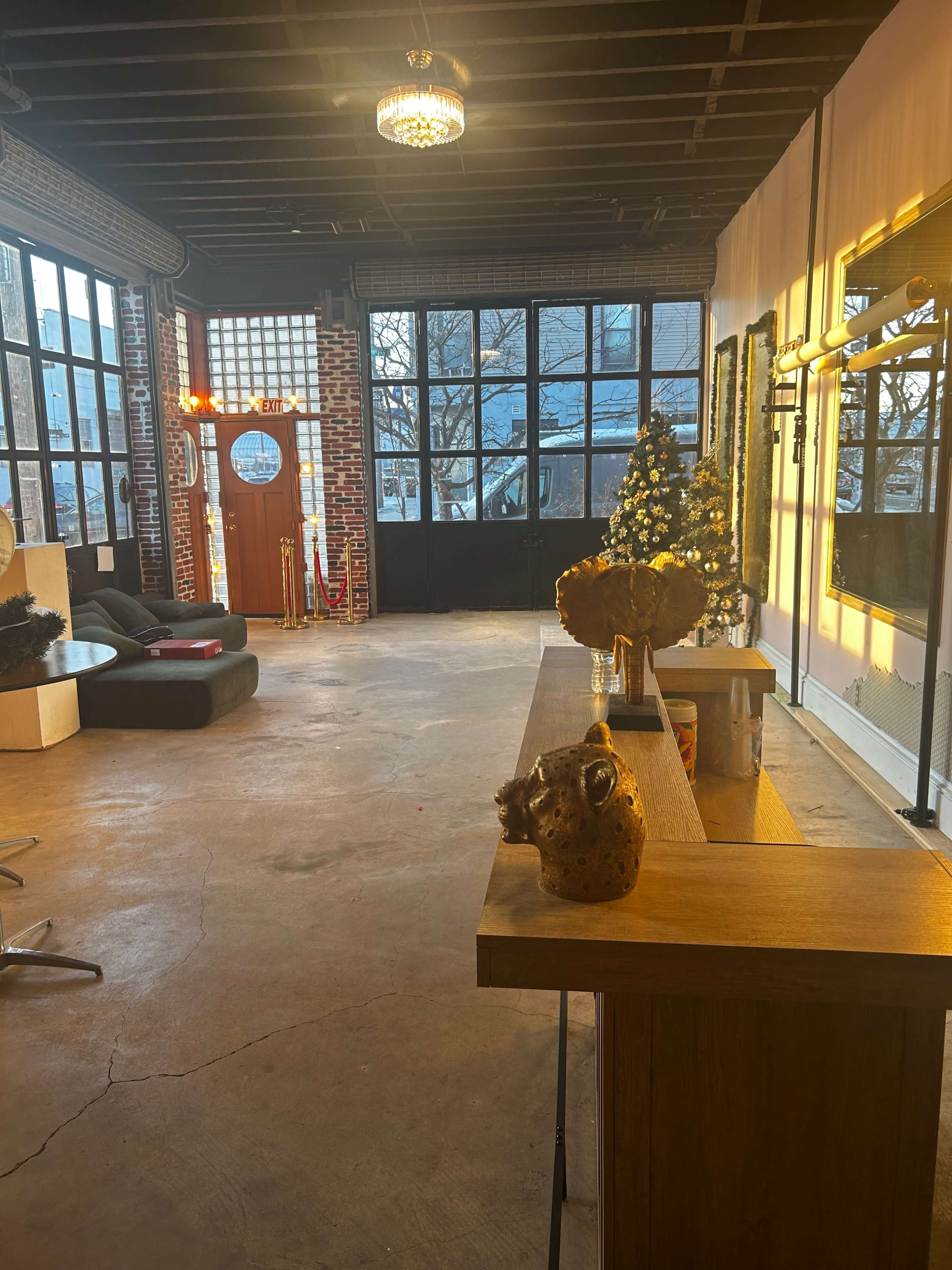 The image shows a spacious room with large windows, a couch, decorative elements, and a bar area.