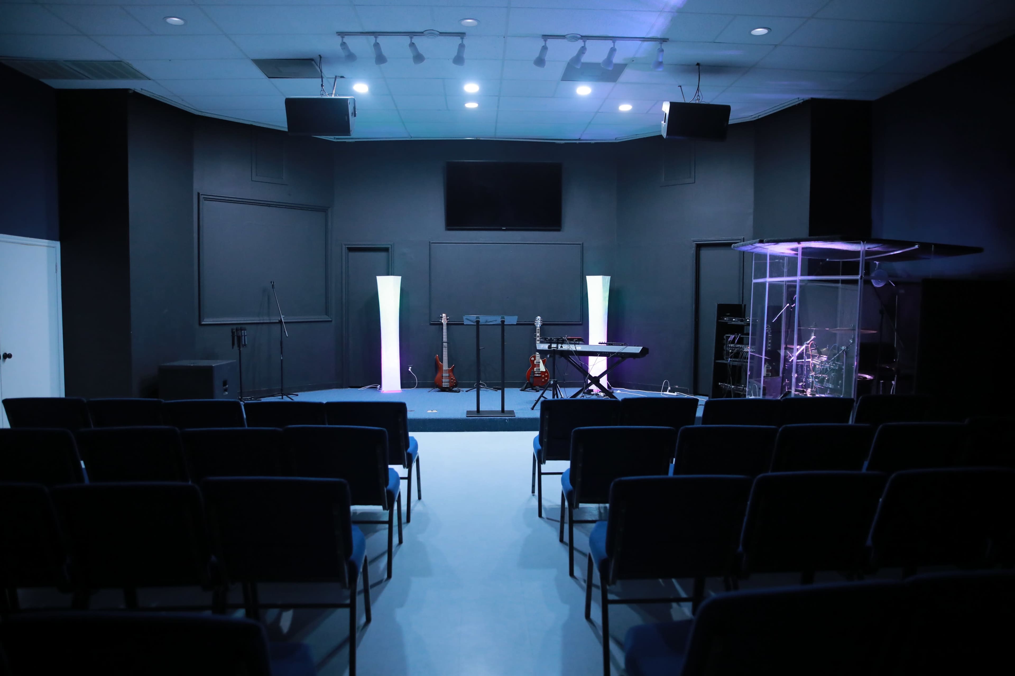 A small auditorium with rows of chairs facing a stage equipped with musical instruments and a transparent sound booth.