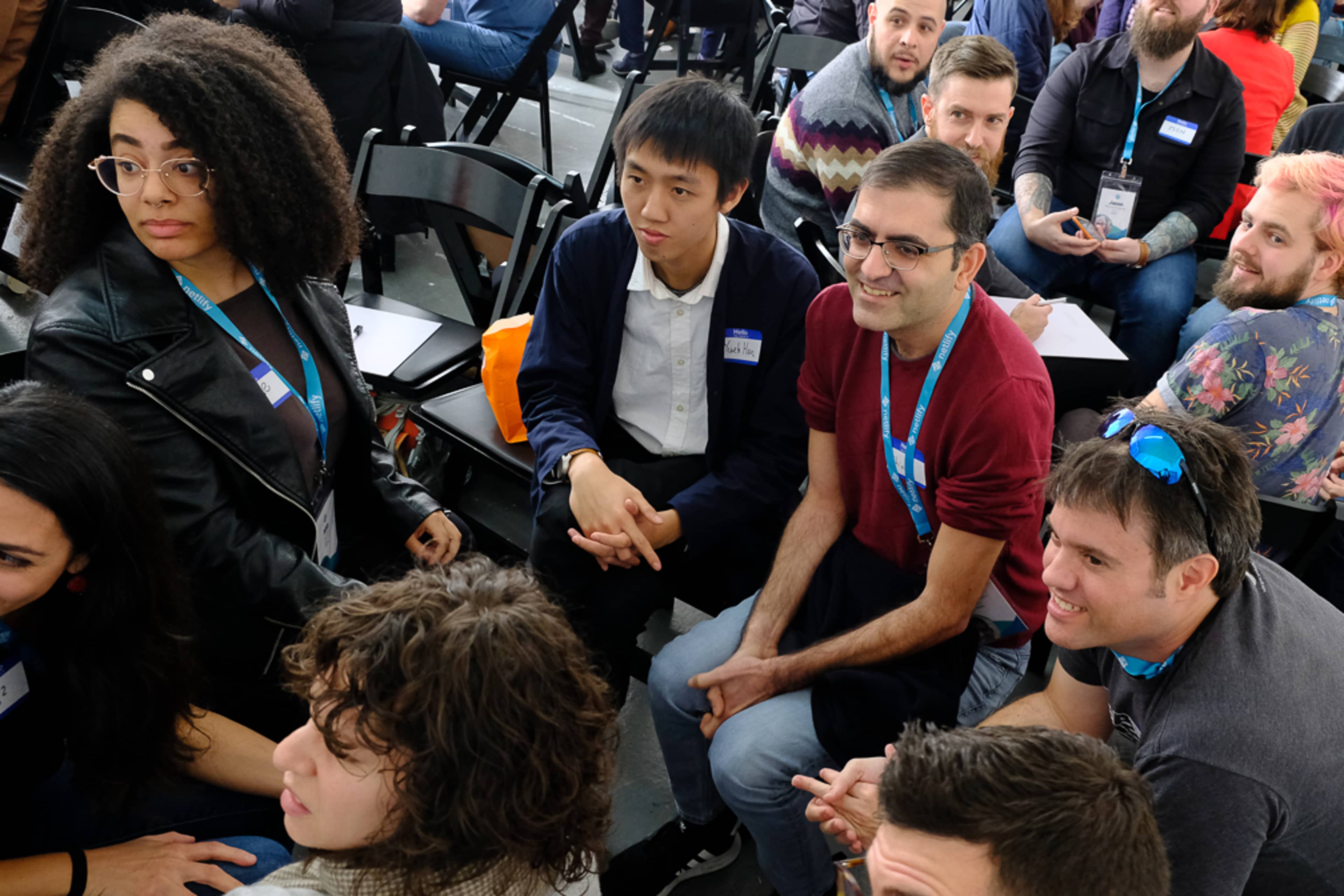 A diverse group of people is seated in a large, open space, engaging in conversation and interaction during a gathering or event.