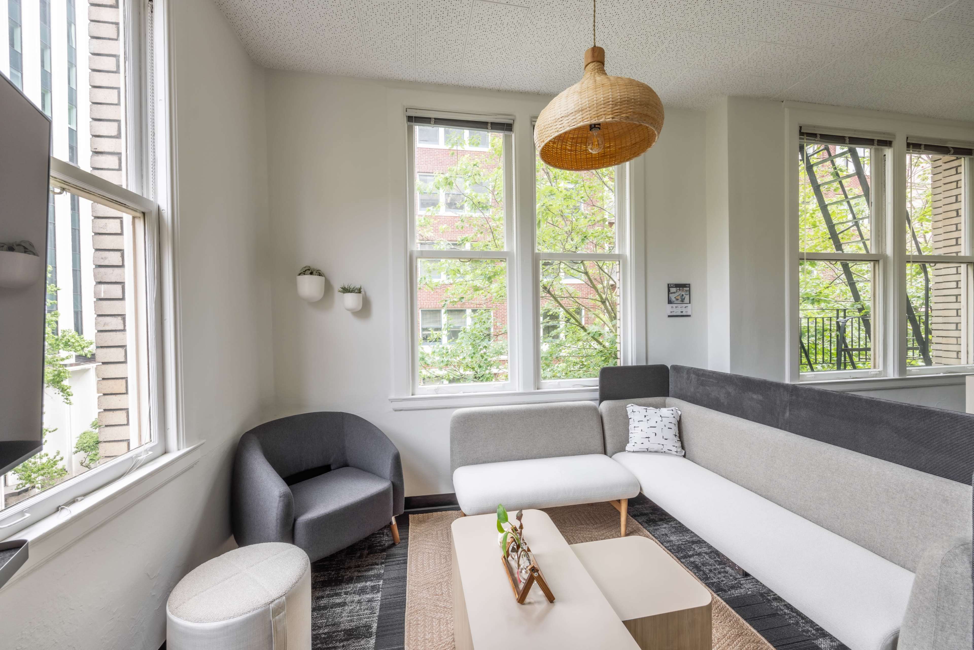 A modern living room with large windows, a gray and white sectional sofa, a round chair, and a coffee table on a patterned rug.