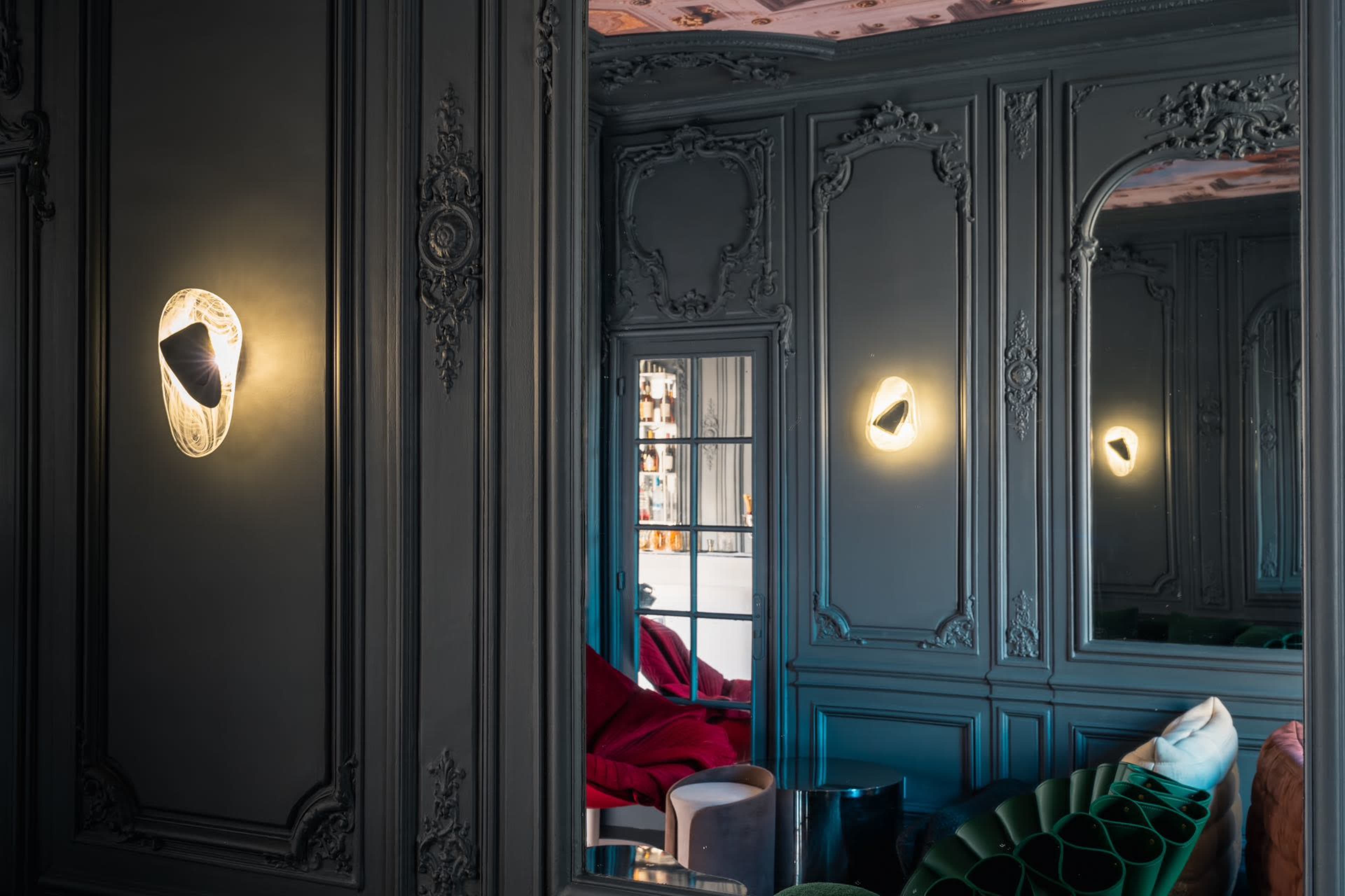 The image shows an elegantly decorated room with ornate green walls, illuminated wall sconces, and a reflection in a large mirror.