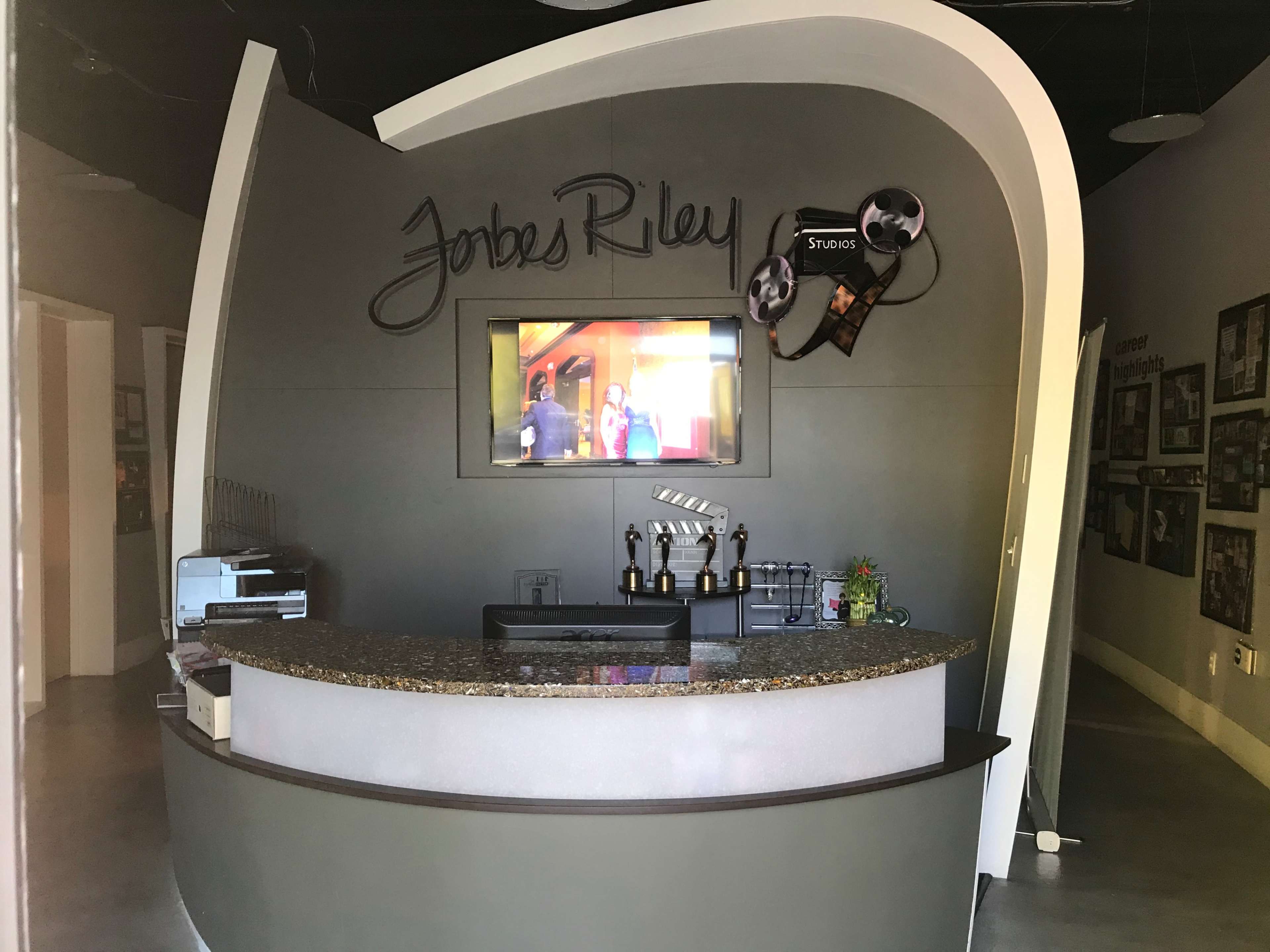 A curved reception desk with a television above it, featuring the name "Jobes Riley" prominently displayed on the wall.