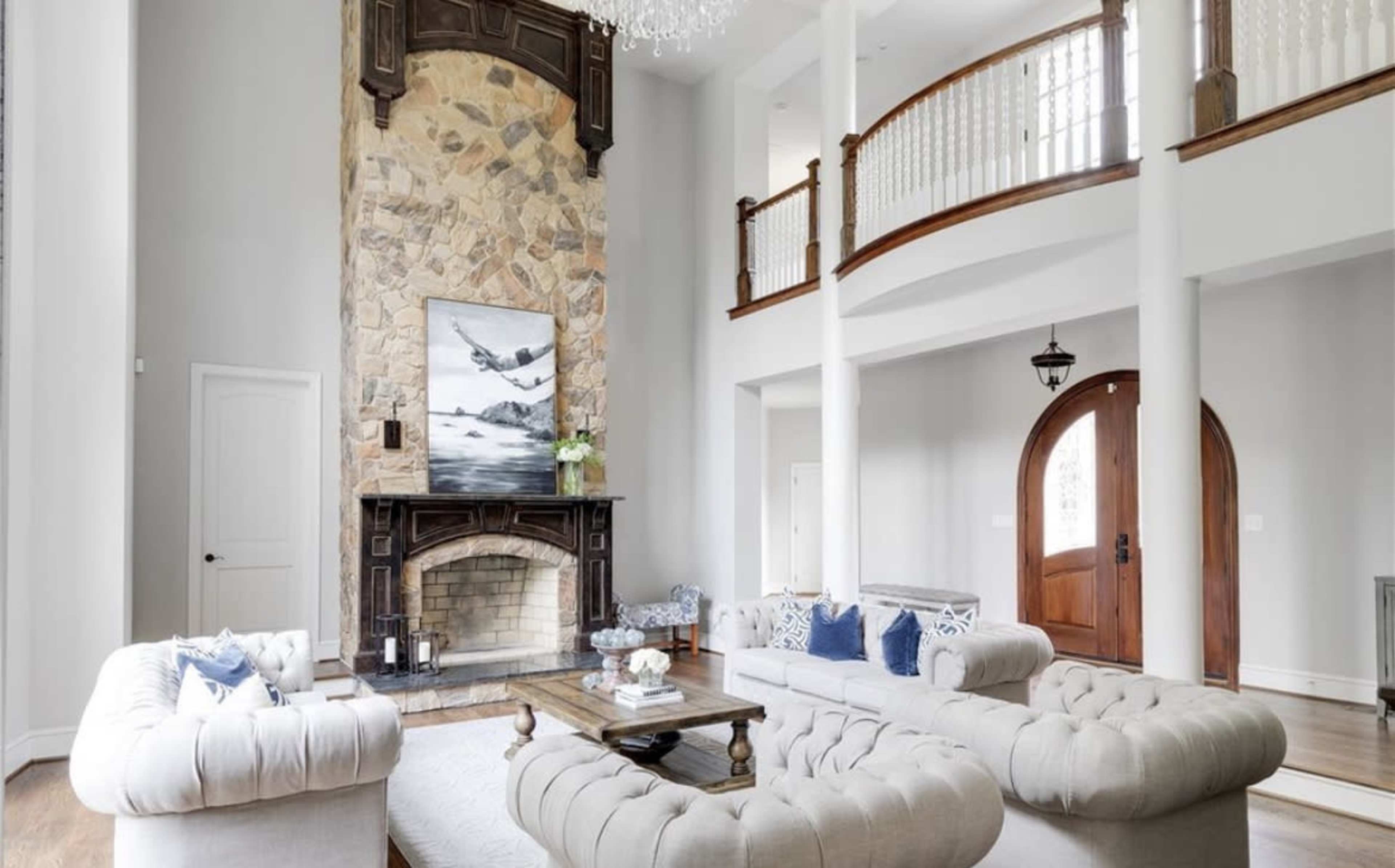 The room features a high ceiling with a stone fireplace at one end, surrounded by large windows and a pair of sofas arranged around a coffee table.