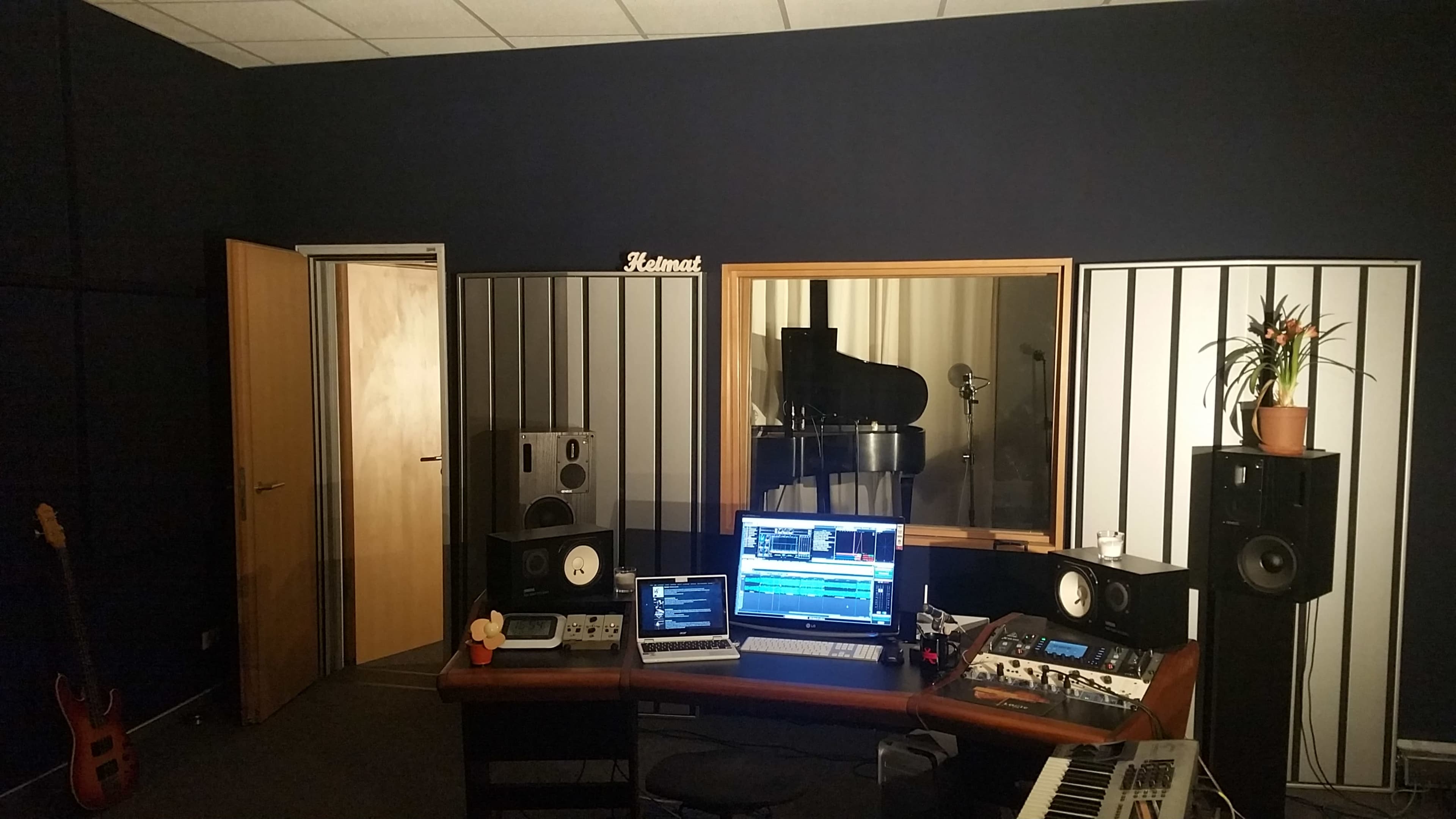A music studio with a piano, mixing equipment, monitors, and a computer setup on a desk.