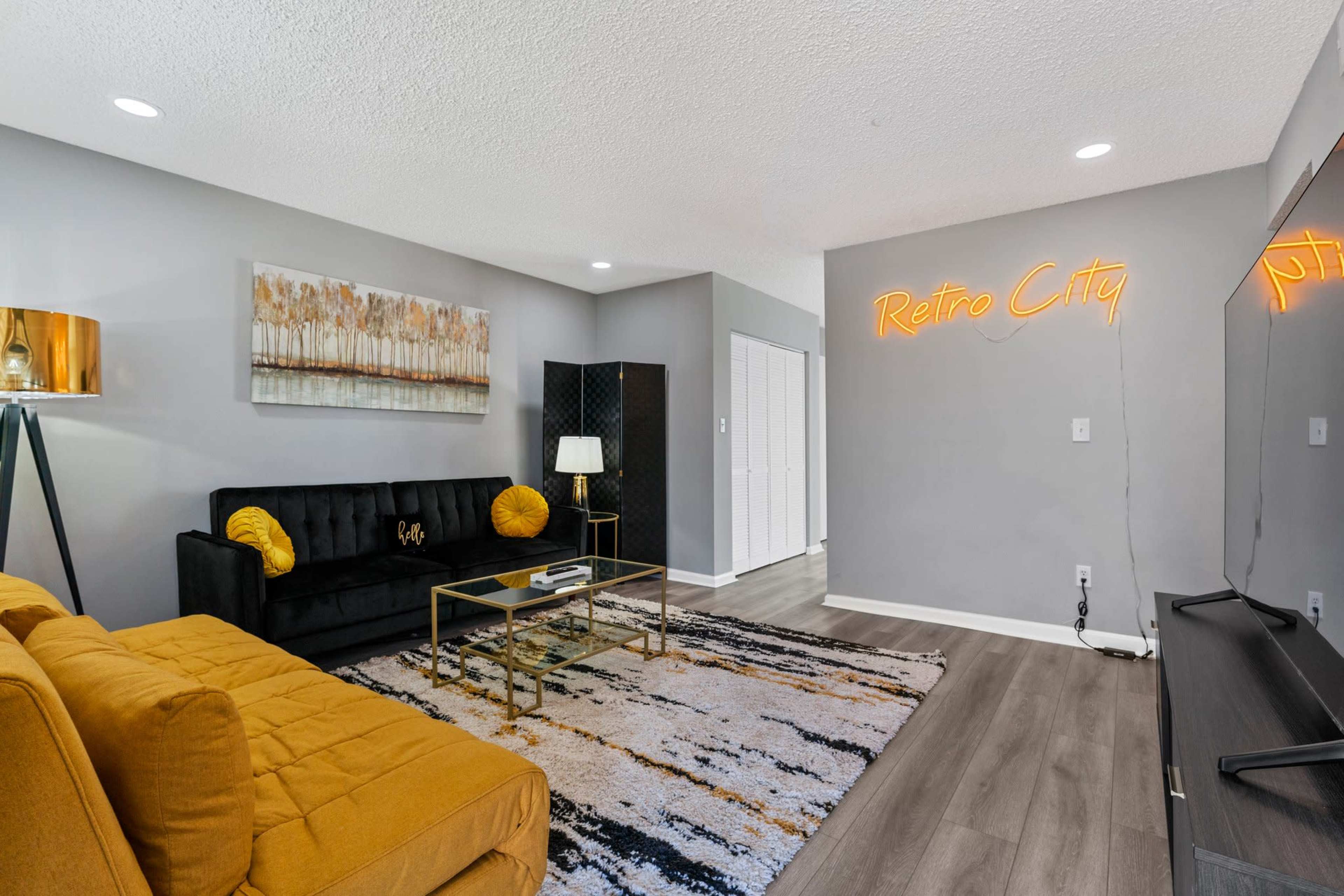 A modern living room with a black sofa, a yellow accent chaise, a gold coffee table, and a neon sign that reads "Retro City" on the wall.