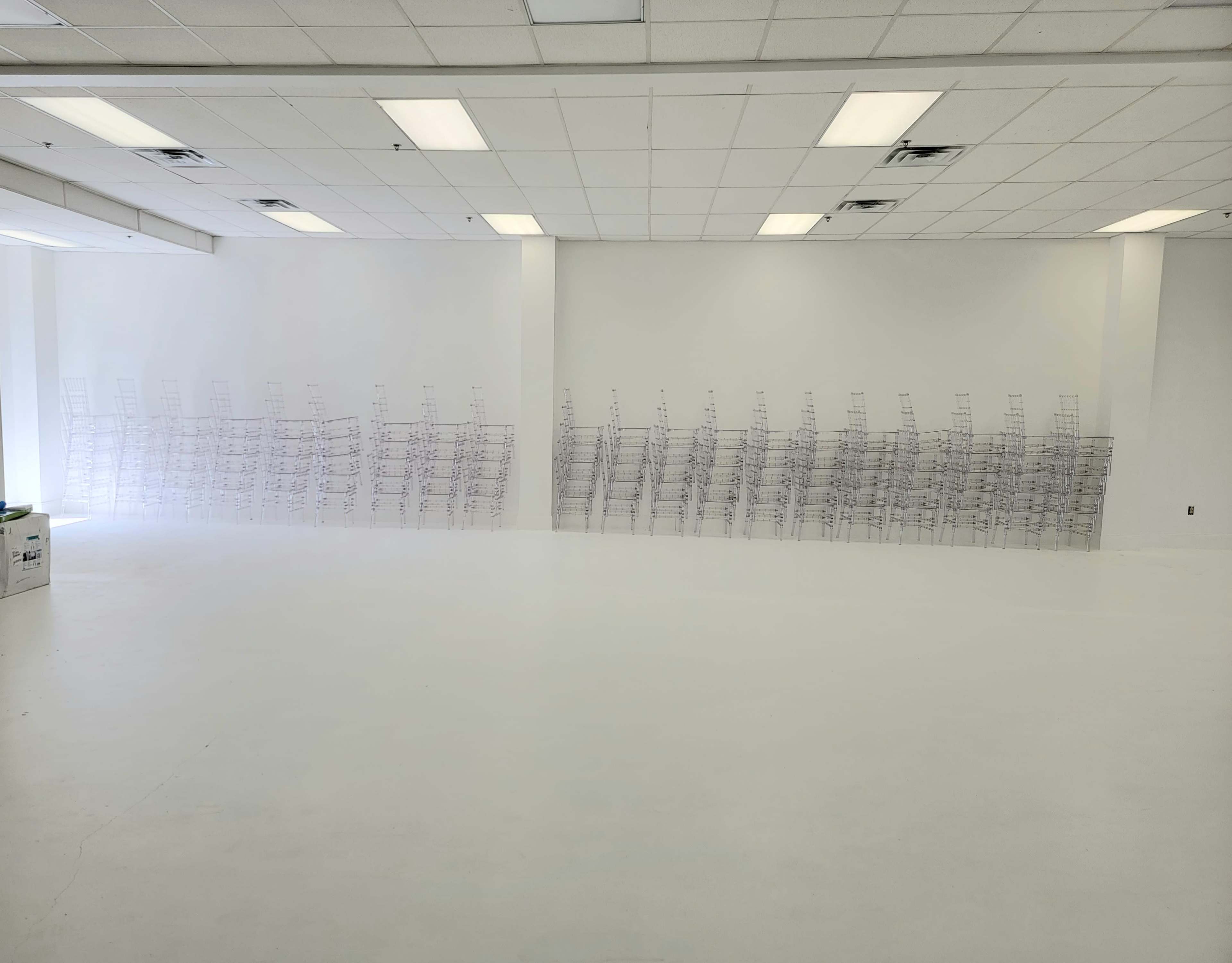 The image shows a spacious room with white walls and a white floor, featuring rows of clear display racks arranged against one wall.