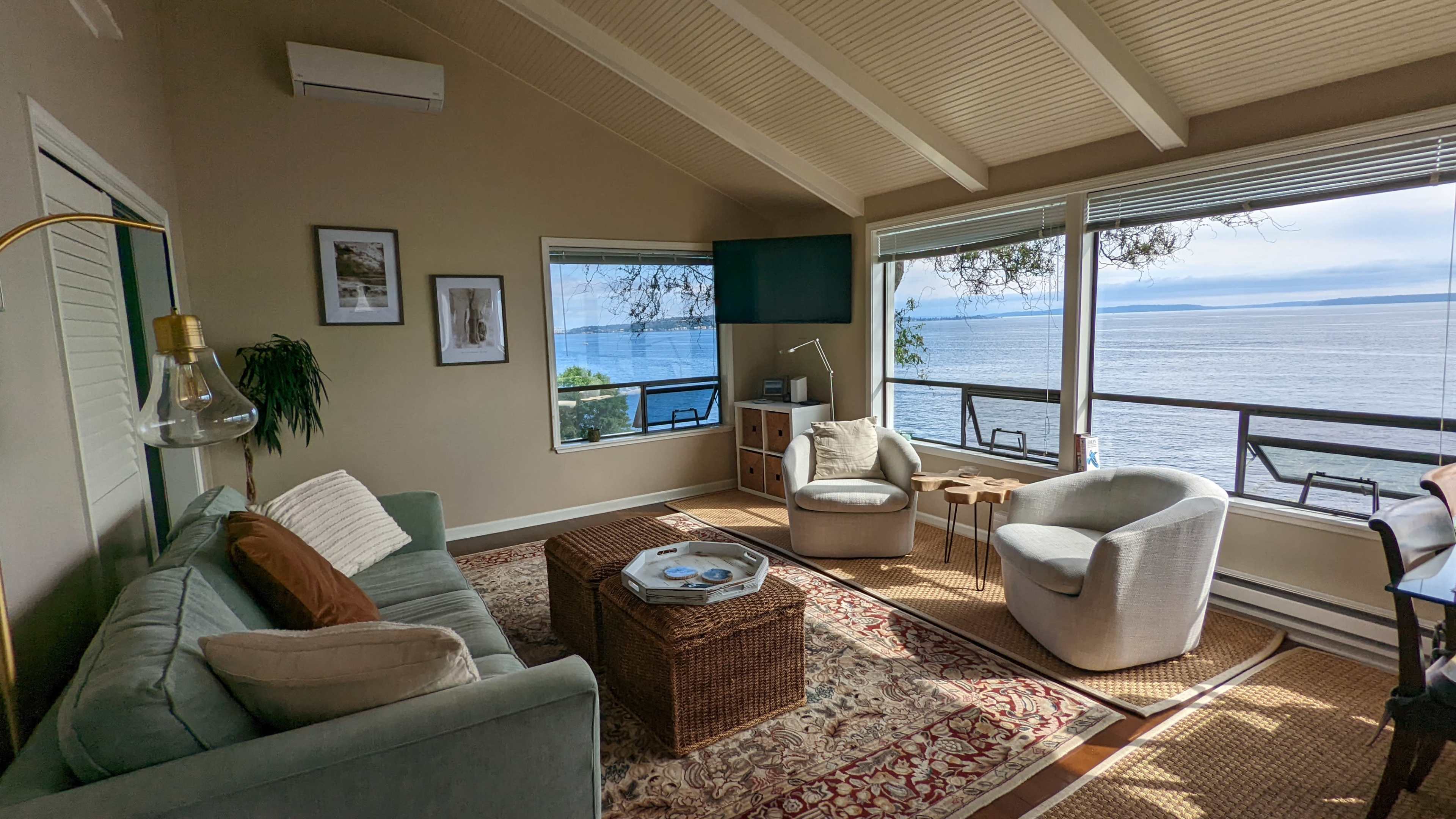 A living room features a couch, two armchairs, a coffee table, and large windows overlooking the ocean.