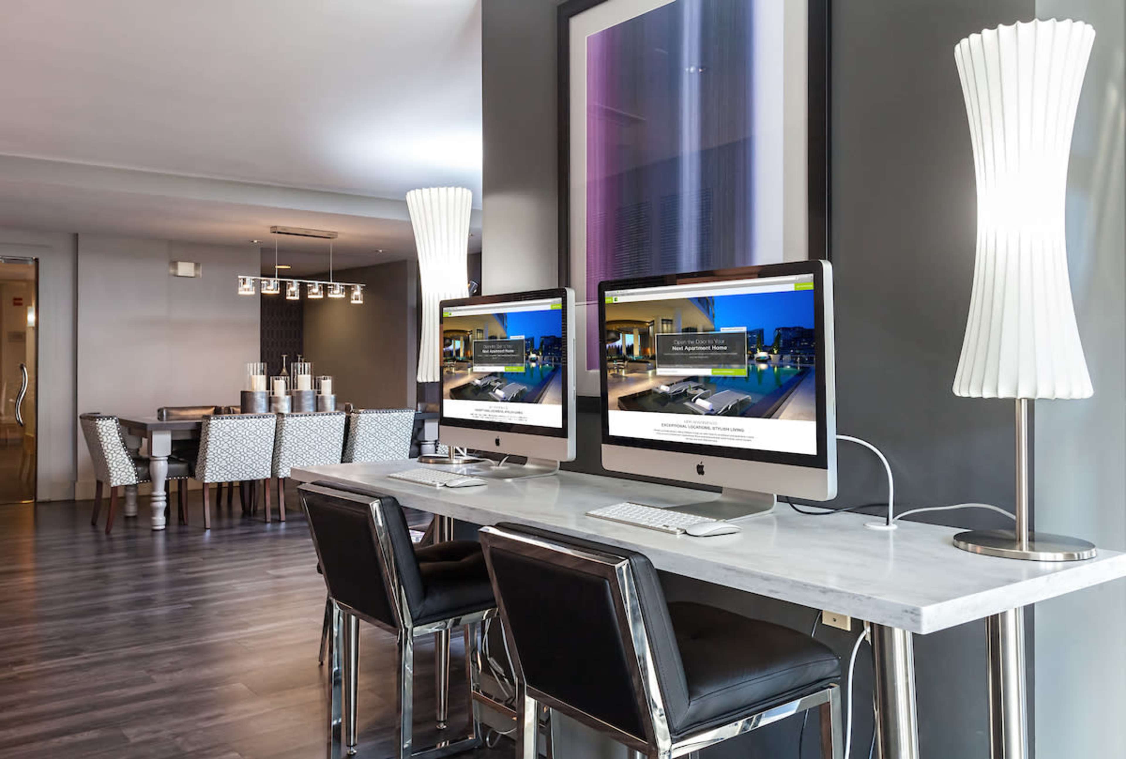 The image shows a modern workspace with two iMacs on a marble desk, surrounded by stylish lamps and a dining area in the background.