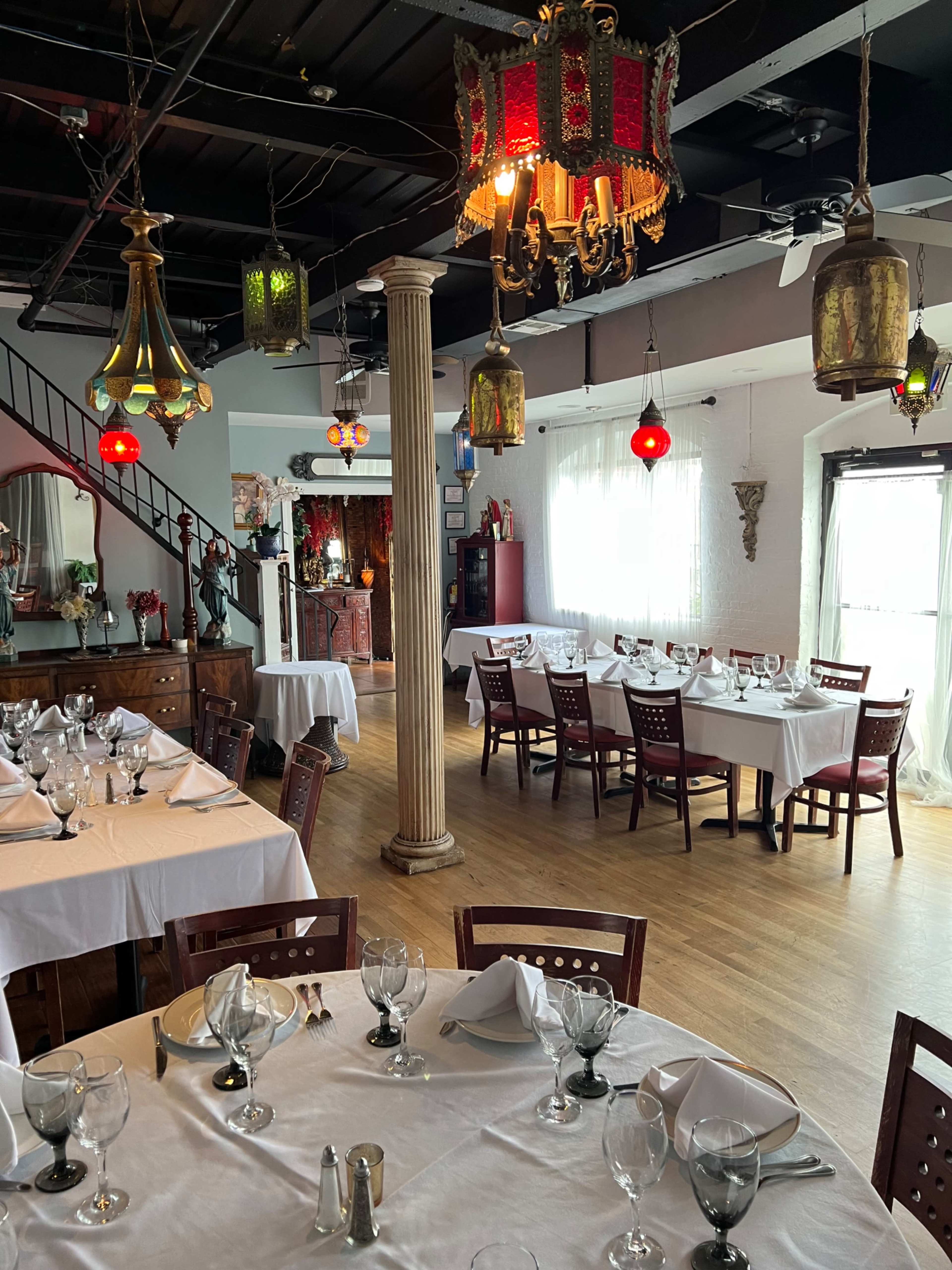 A dining area of a restaurant with multiple white-covered tables set with glassware and a variety of hanging light fixtures.