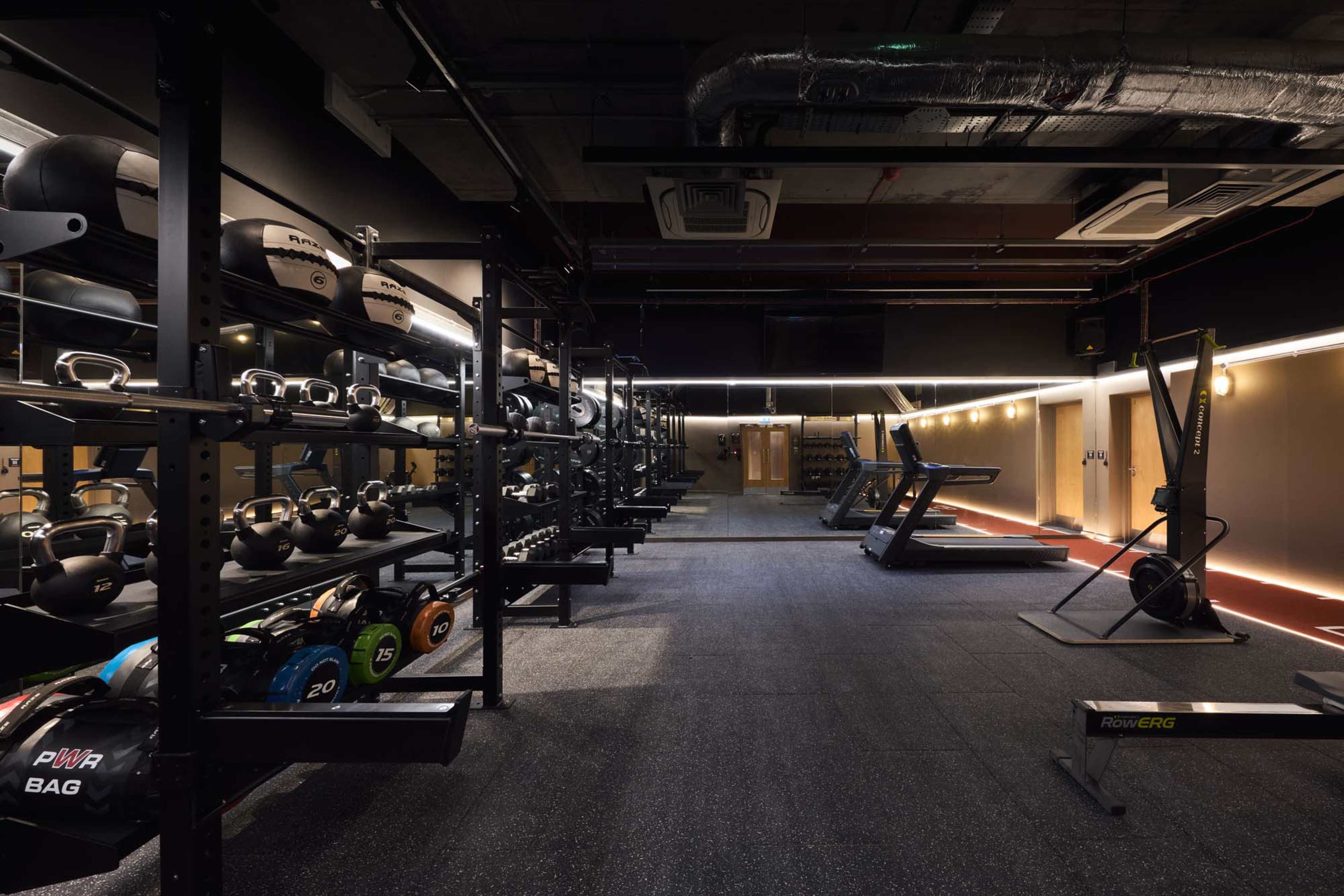 The image shows a modern gym interior equipped with various weightlifting and fitness machines, neatly organized kettlebells, and a rubberized floor.