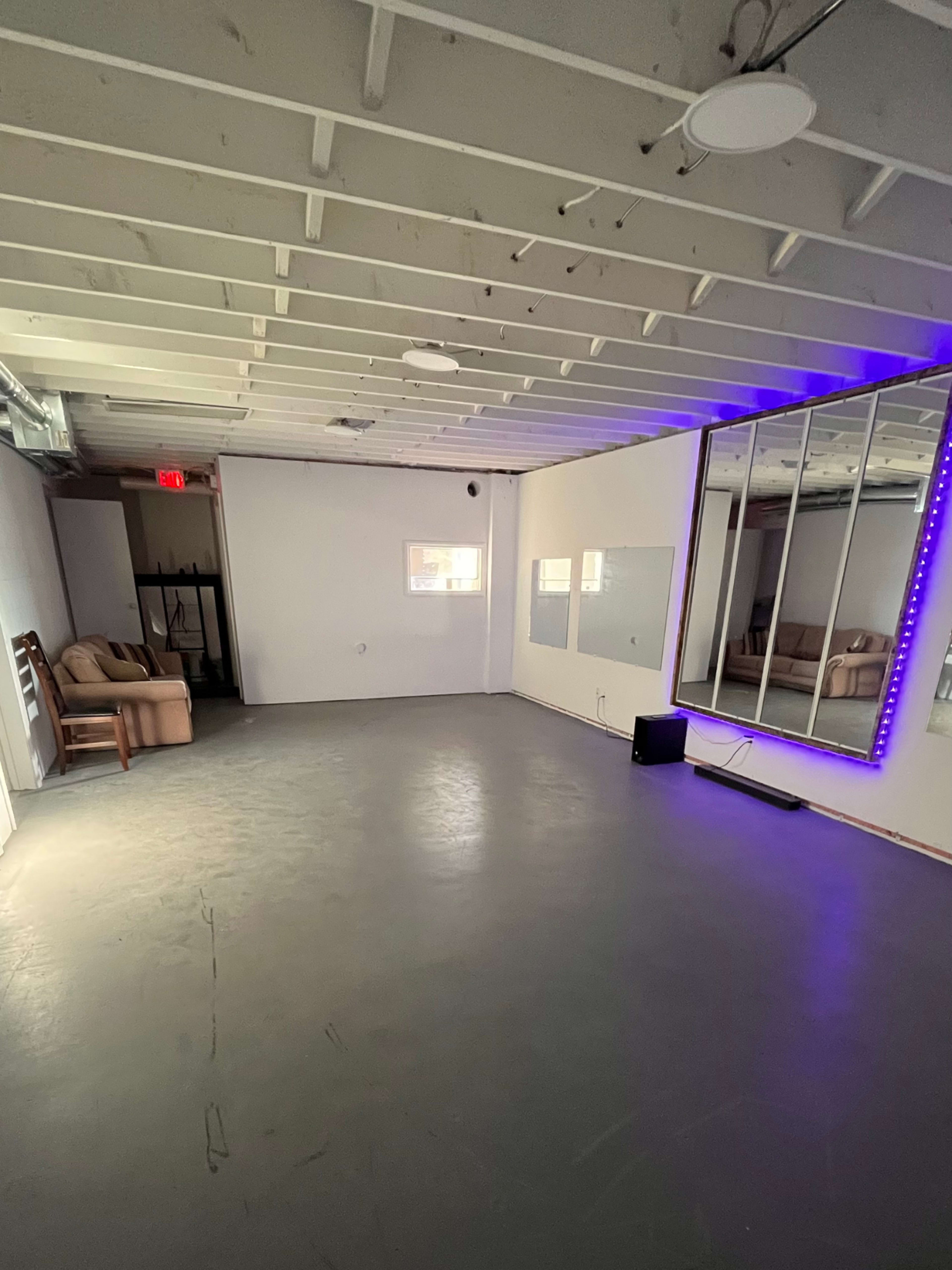 A spacious, empty room with a concrete floor, a mirrored wall, and a couch in the corner.