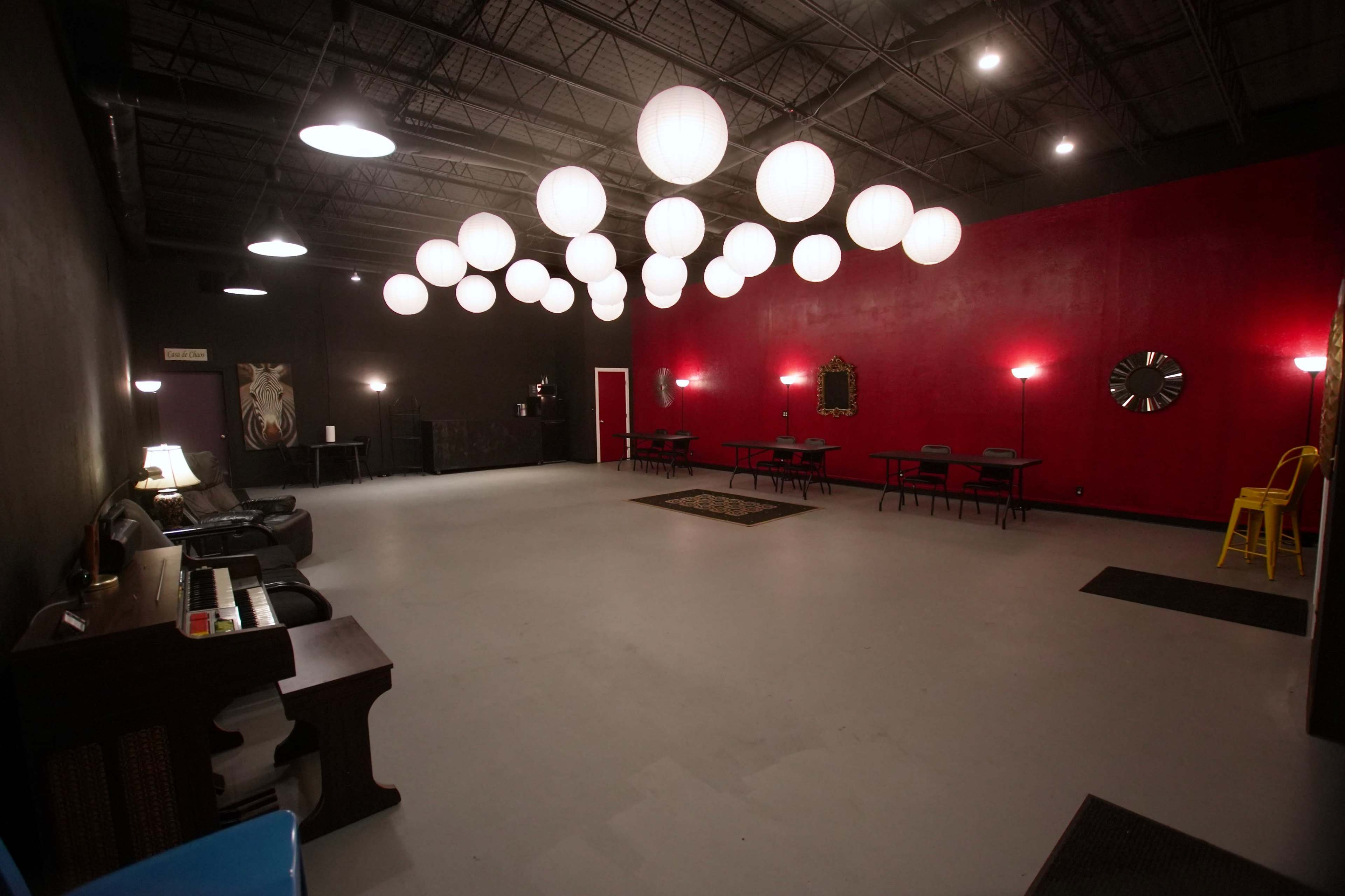A spacious indoor area with a gray floor, red and black walls, and several round hanging lamps illuminating the space.