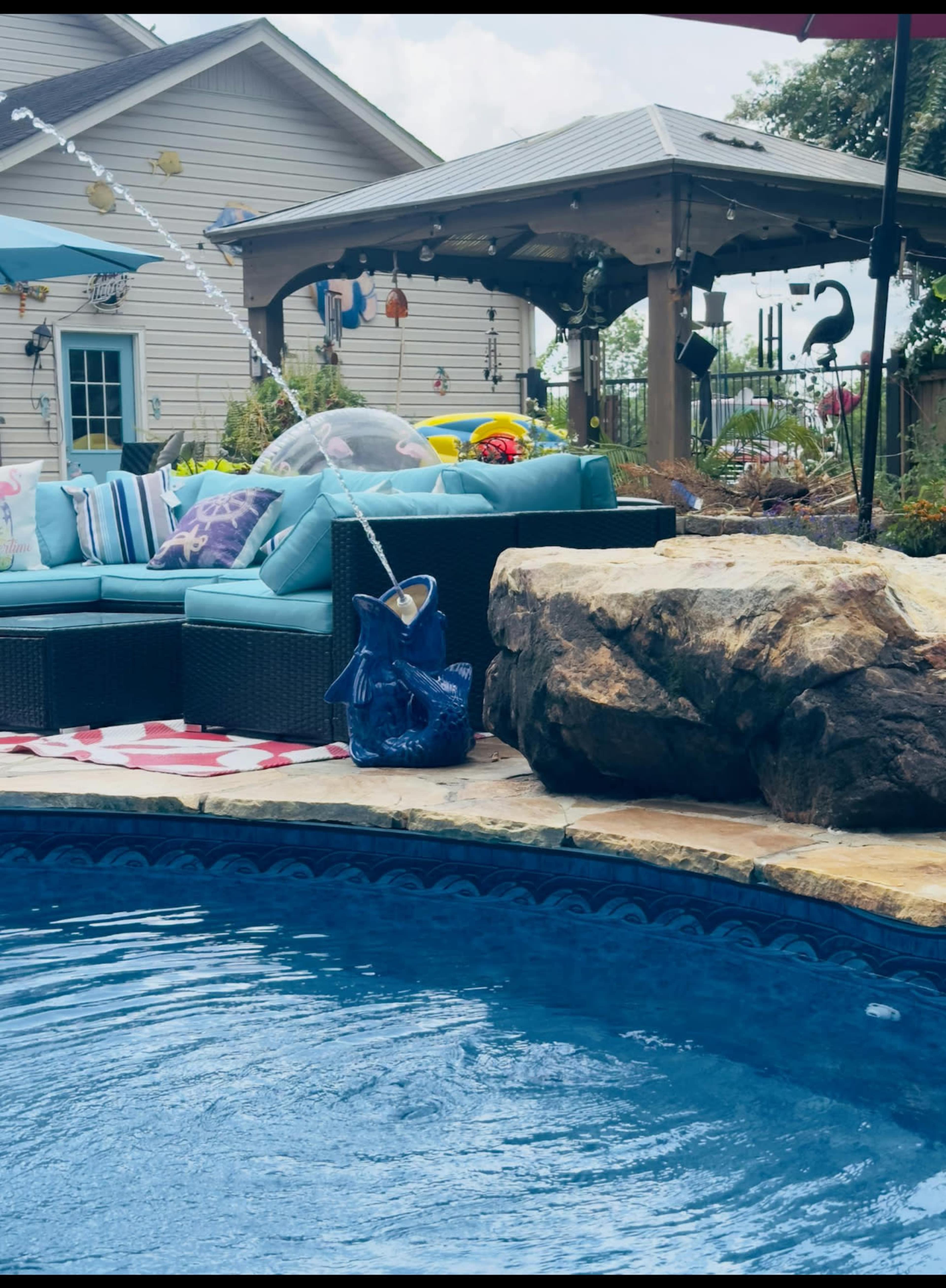 A spacious outdoor area features a blue sectional sofa, a rock water feature, and a swimming pool surrounded by colorful toys and decorations.