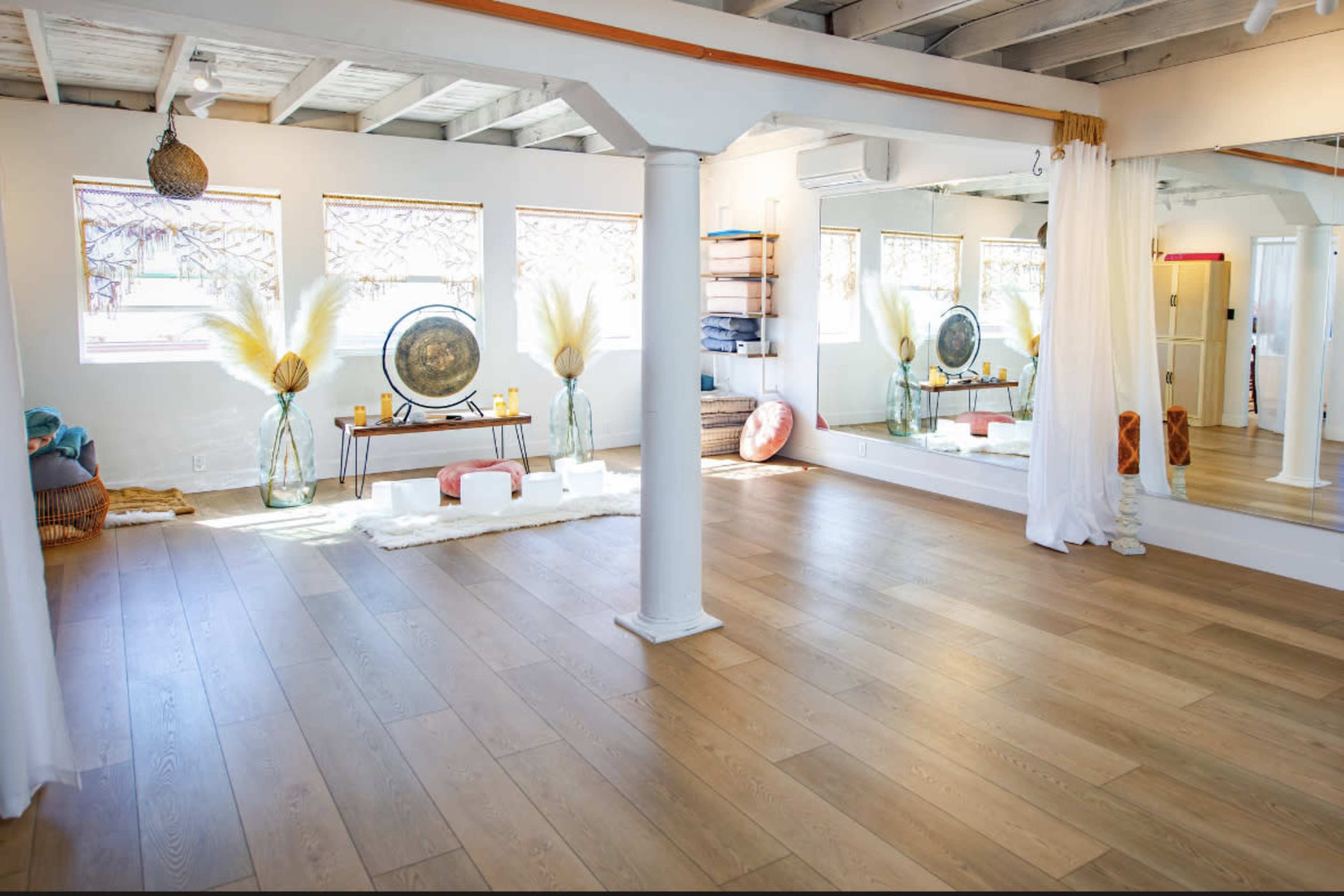 A spacious, well-lit room featuring wooden floors, large mirrors, and decorative items like vases and cushions.