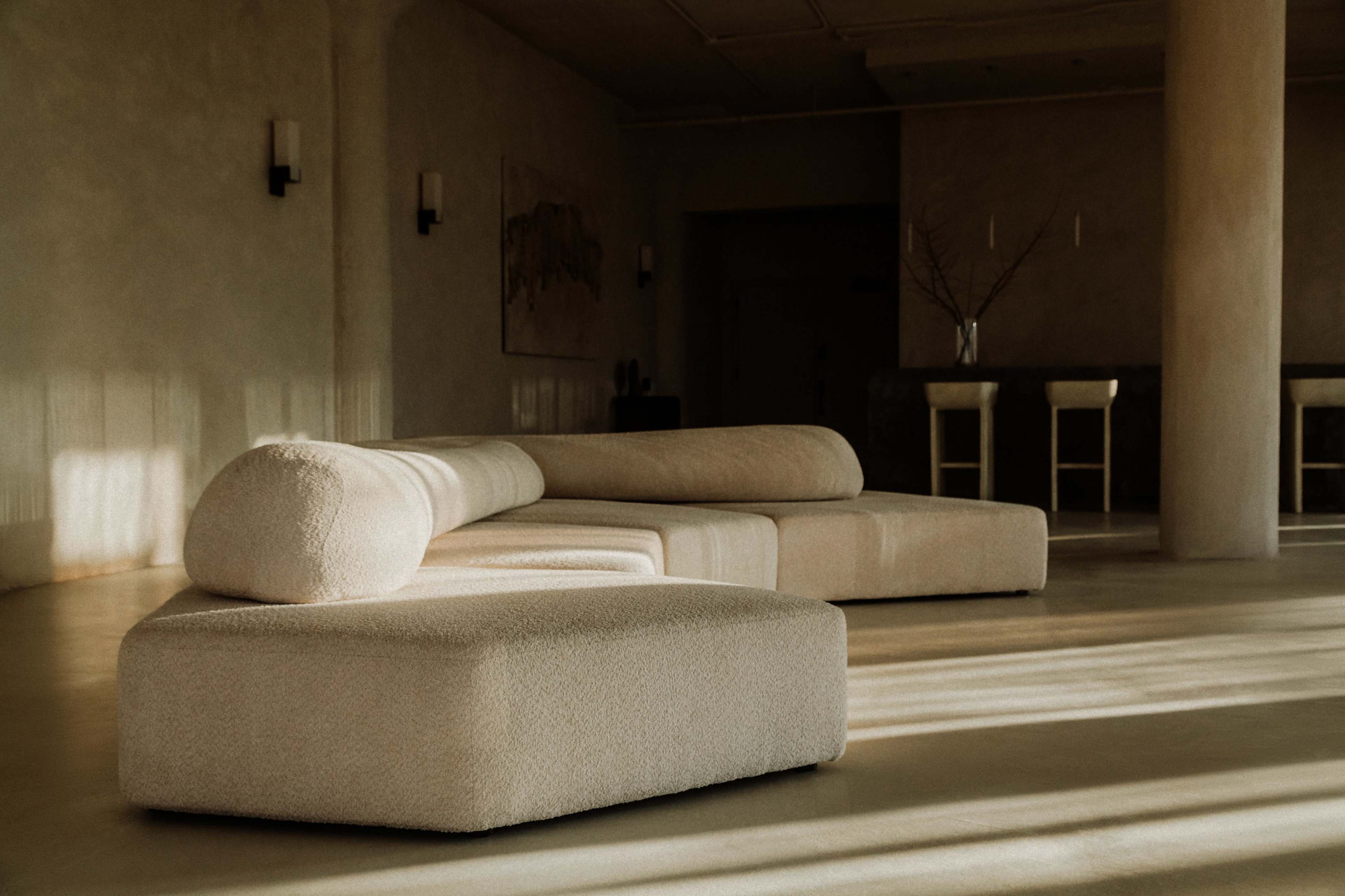 A light-filled interior features a large, beige sectional sofa with a rounded end on a polished floor.