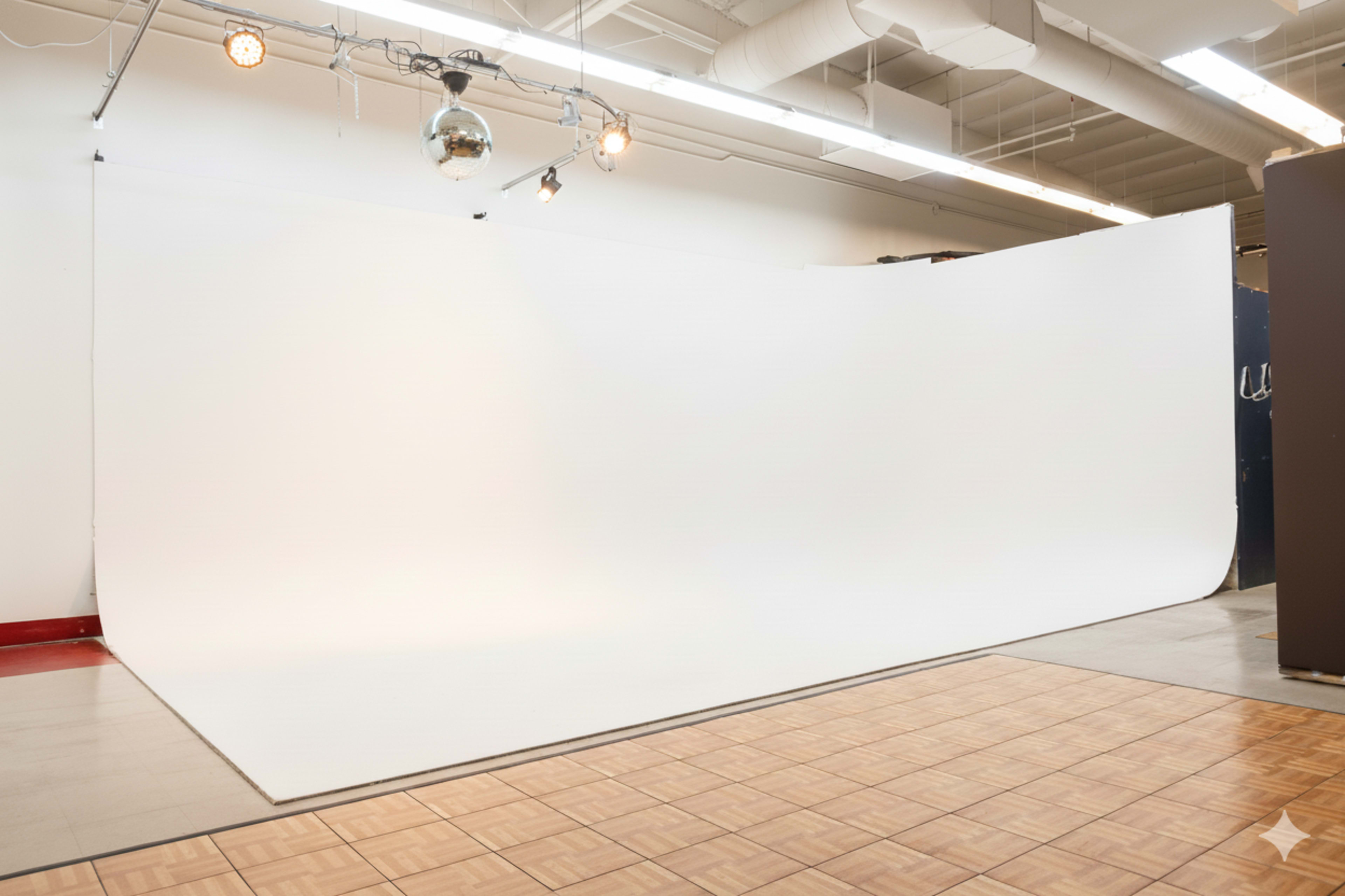 The image shows a spacious studio with a white backdrop curved at the edges and a wooden floor.
