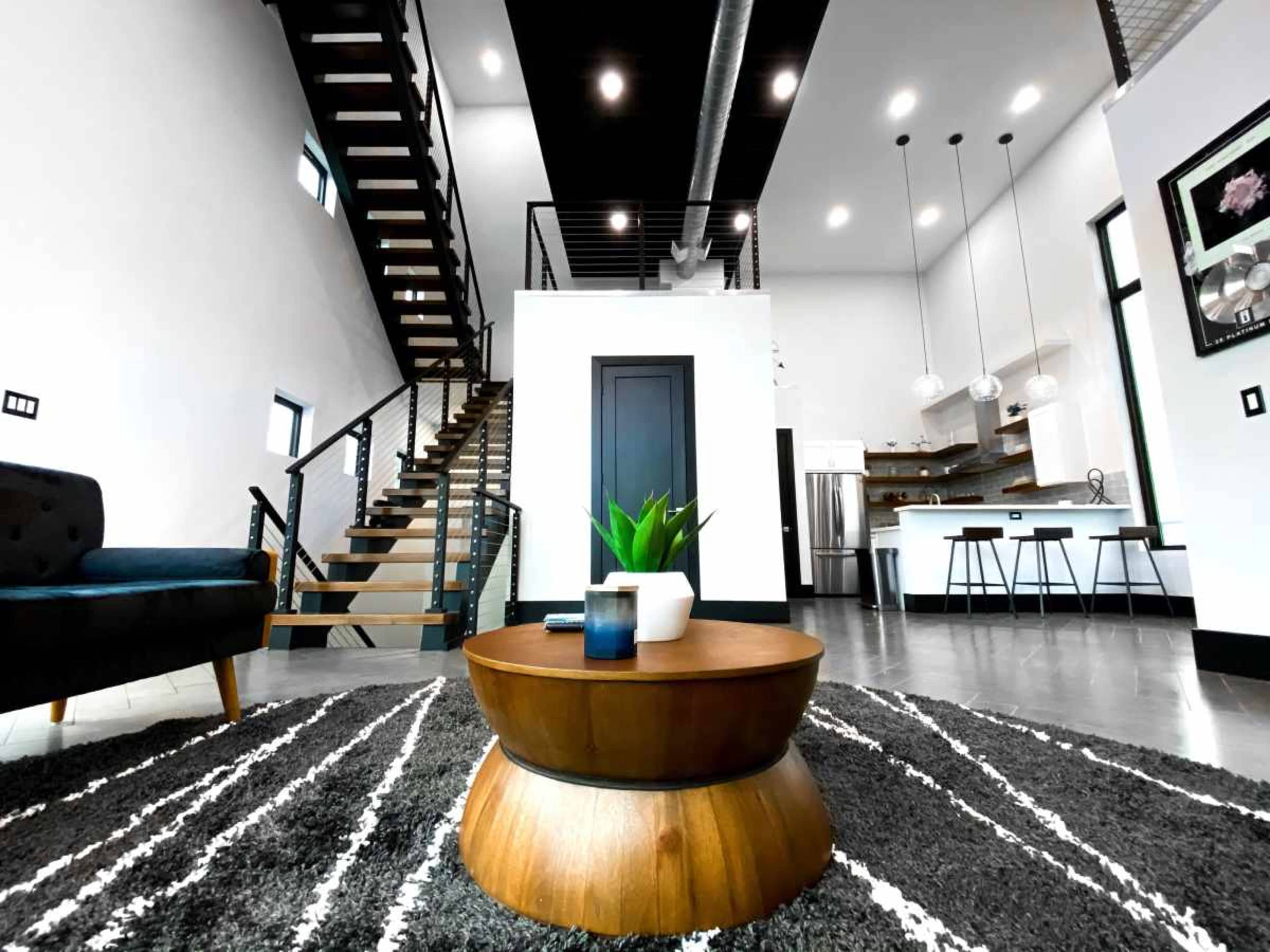 The image shows a modern interior of a home featuring a staircase, a coffee table with decorative items, and a spacious kitchen area in the background.