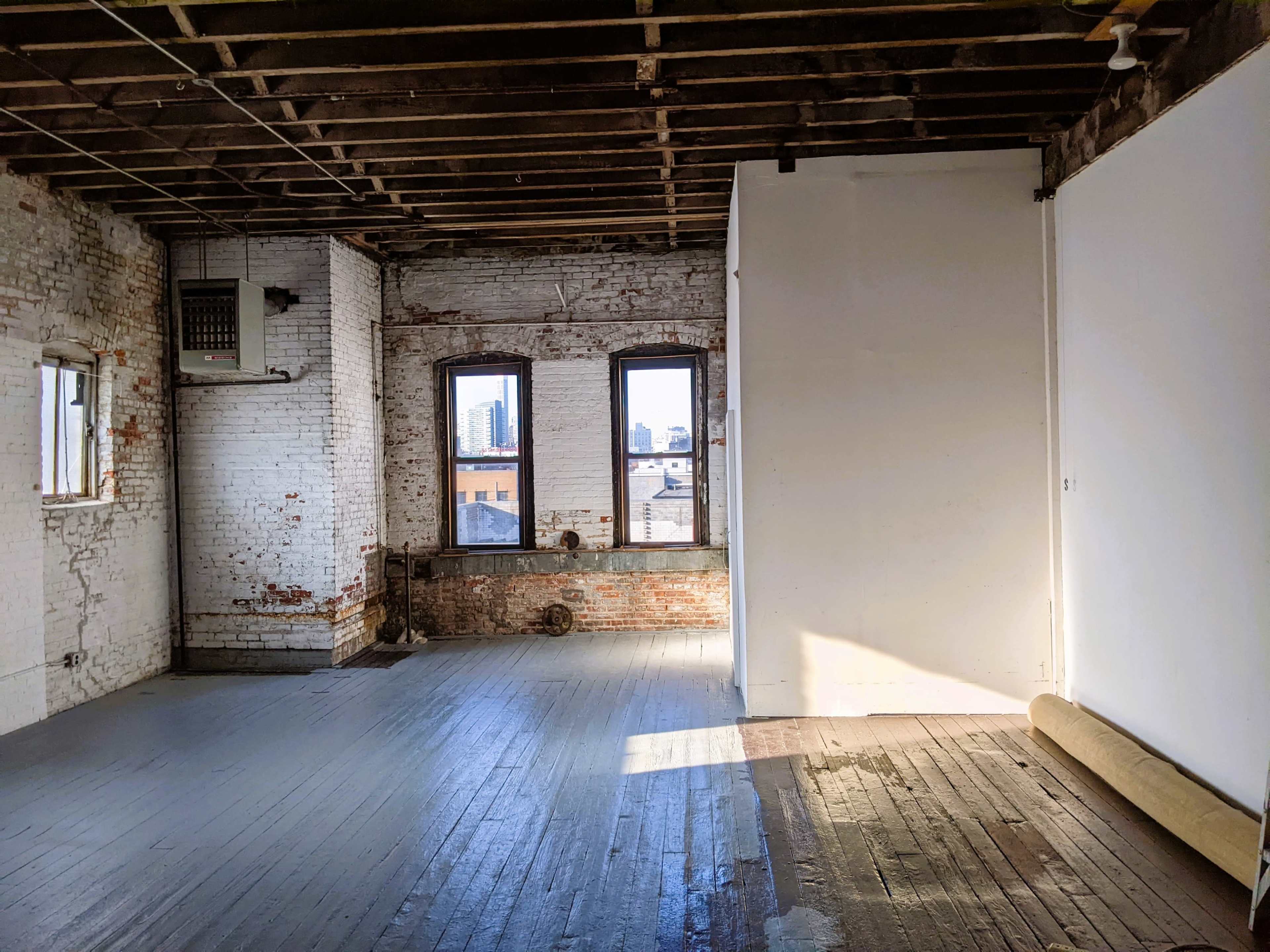 An empty industrial space features exposed brick walls, large windows with a city view, and wooden flooring.