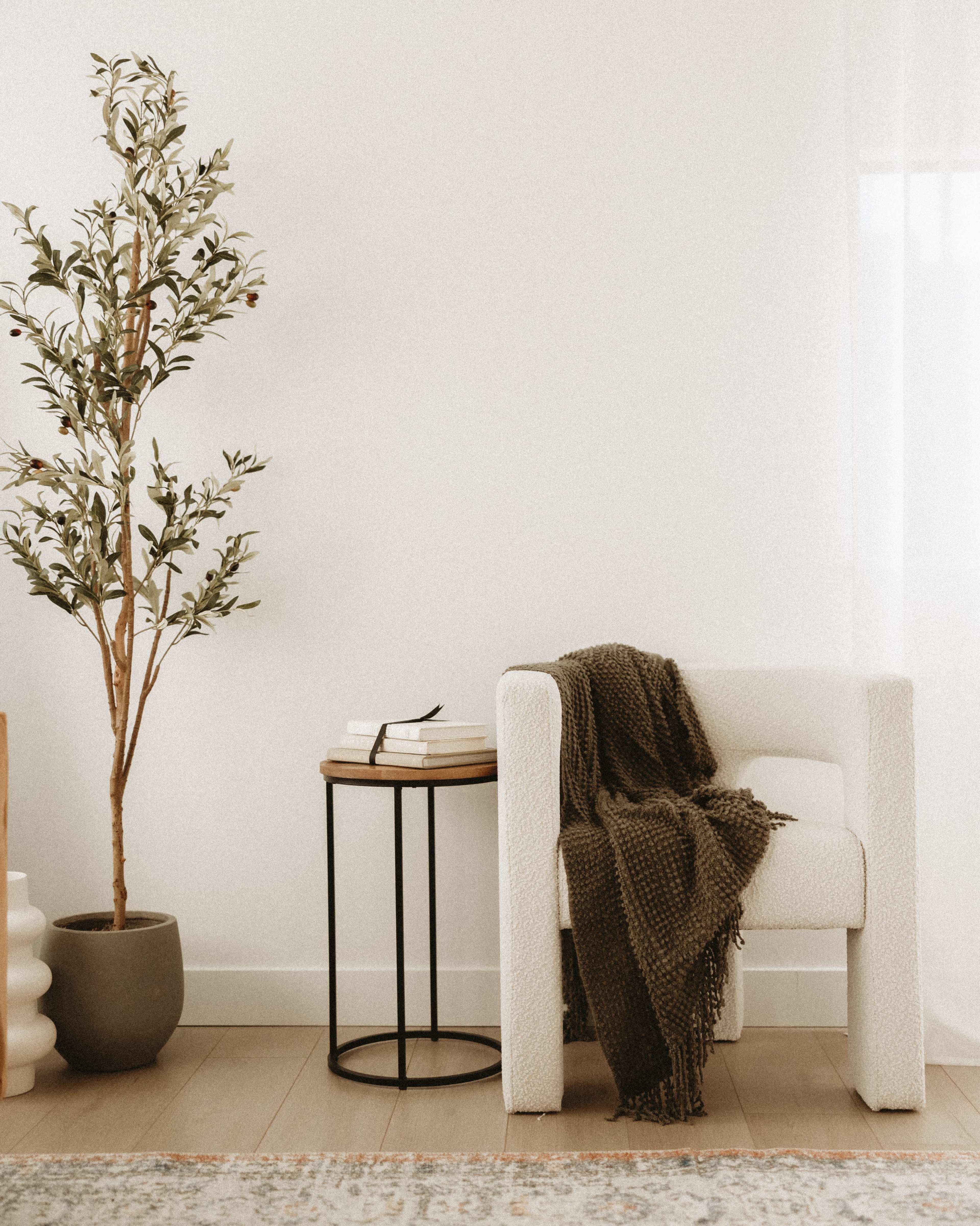 A modern chair with a blanket draped over it is positioned next to a small table holding a stack of books and a potted plant.
