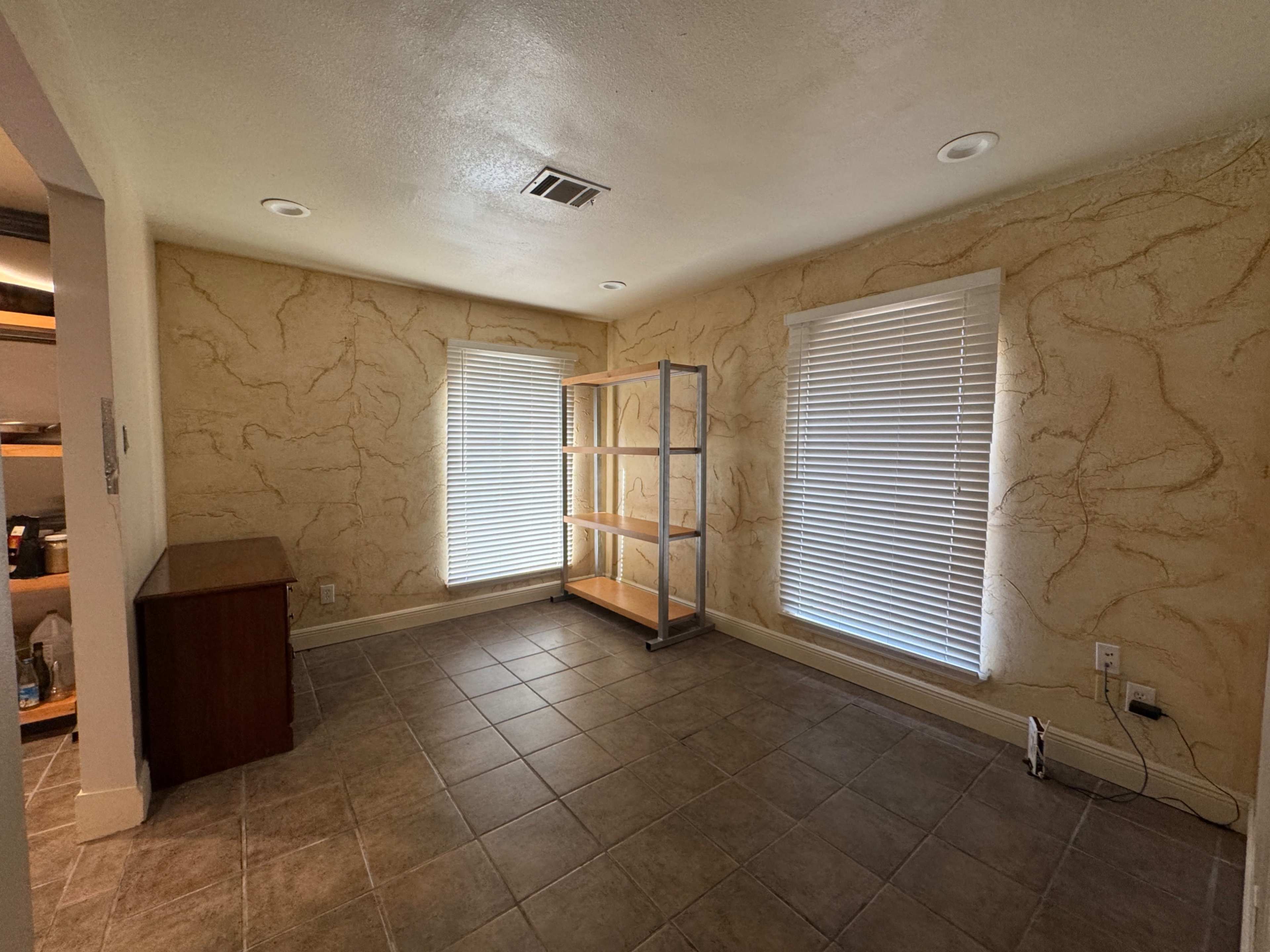 The room features two windows with blinds, a shelving unit against one wall, and tiled flooring.
