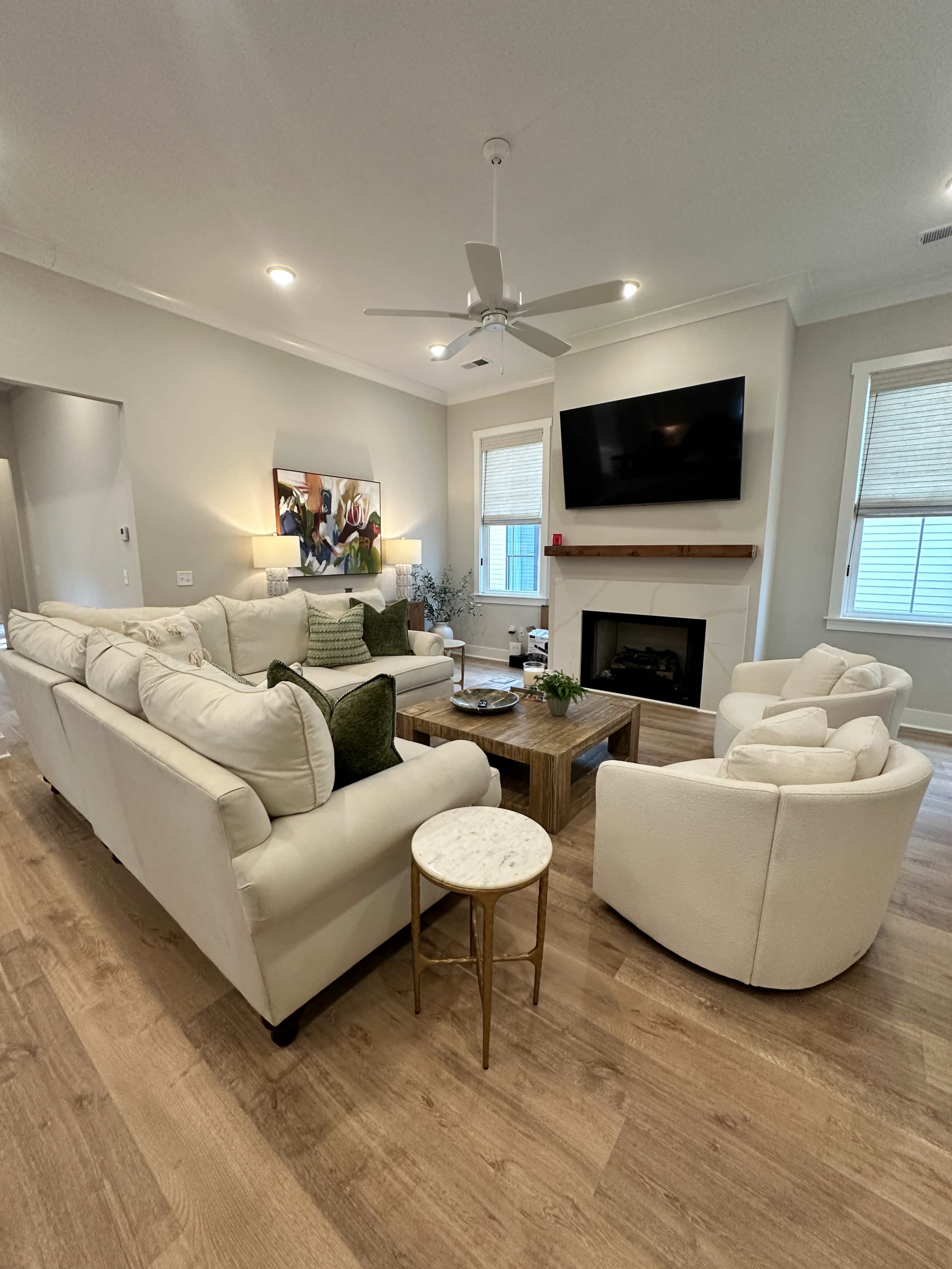 The image shows a spacious living room featuring a large sectional sofa, two armchairs, a coffee table, a fireplace, and a wall-mounted television.