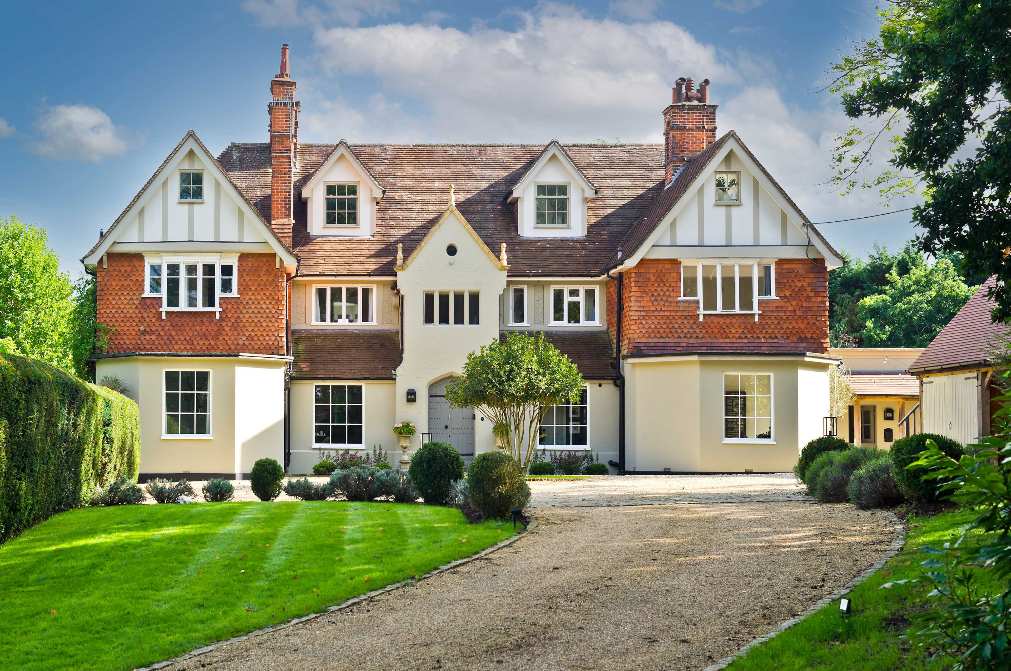 A large, two-story house with a symmetrical facade, characterized by a mix of red brick and white clapboard, set in a landscaped yard with neatly trimmed hedges and a gravel driveway.