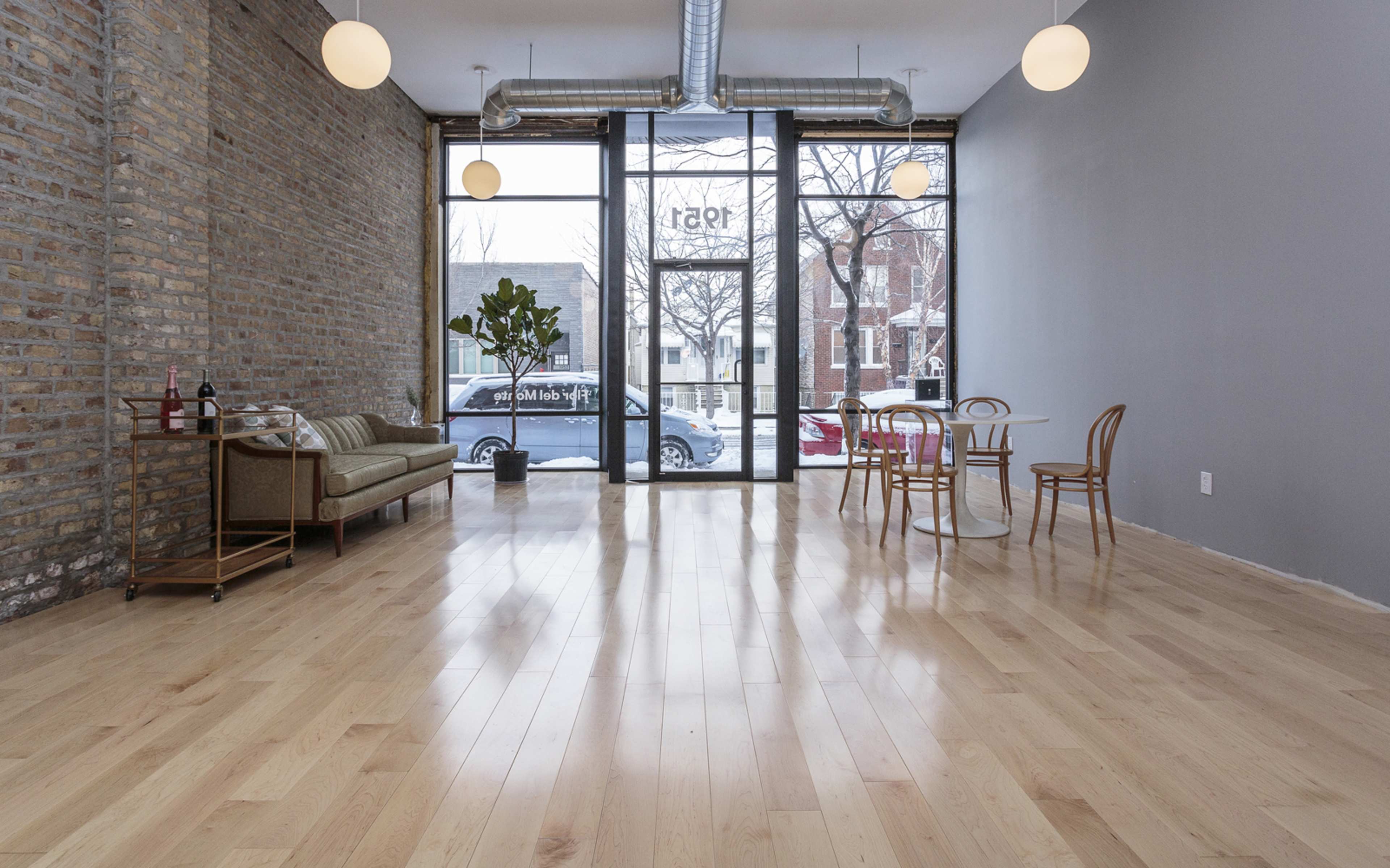 A spacious, empty room with hardwood floors, large windows, and a mix of modern furniture including a sofa, dining table, and chairs.