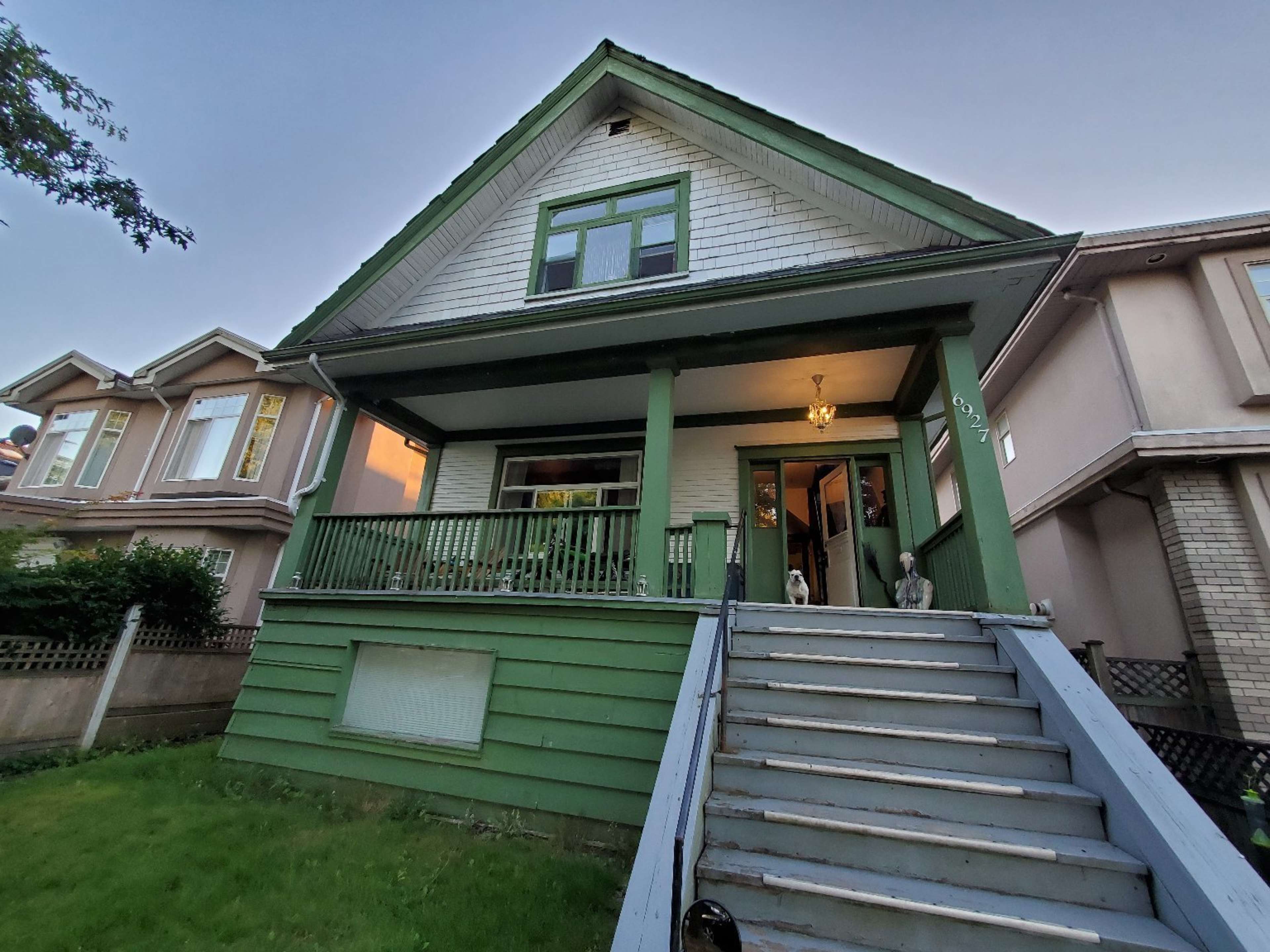 A green, two-story house with a front porch and white shingle accents is visible, surrounded by well-maintained lawns and neighboring homes.