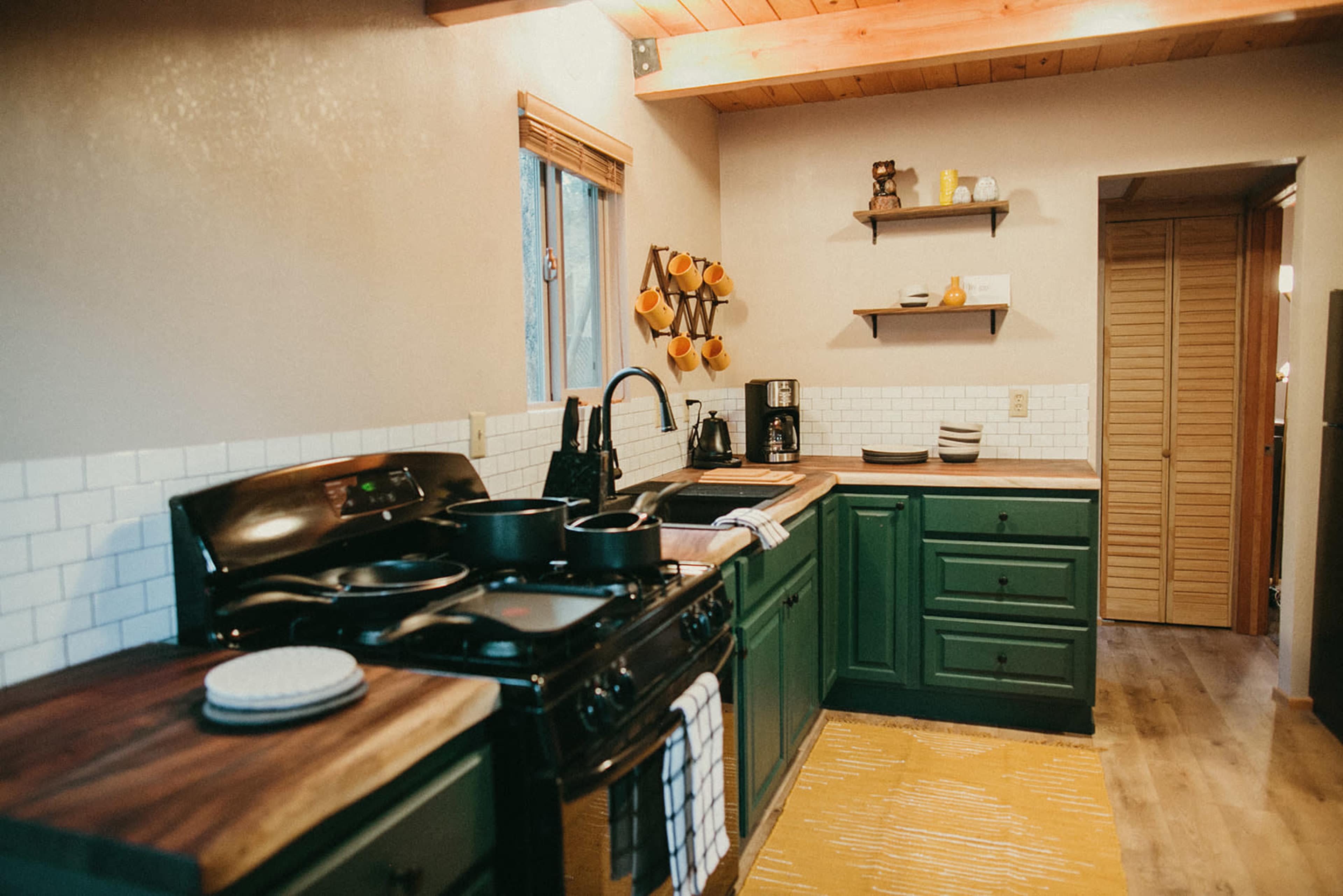 The kitchen features dark green cabinets, a wooden counter, and a black stove with utensils and dishware neatly arranged.