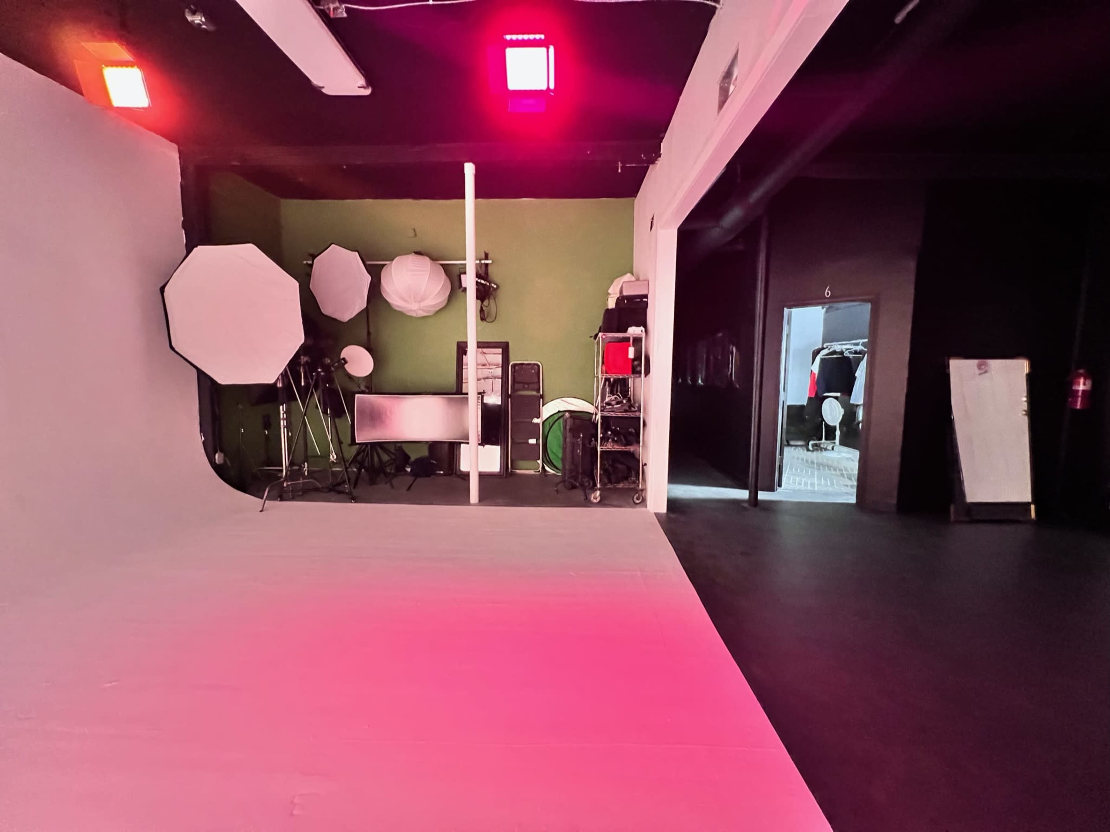 A photography studio with a green accent wall, lighting equipment, and a large white floor area.