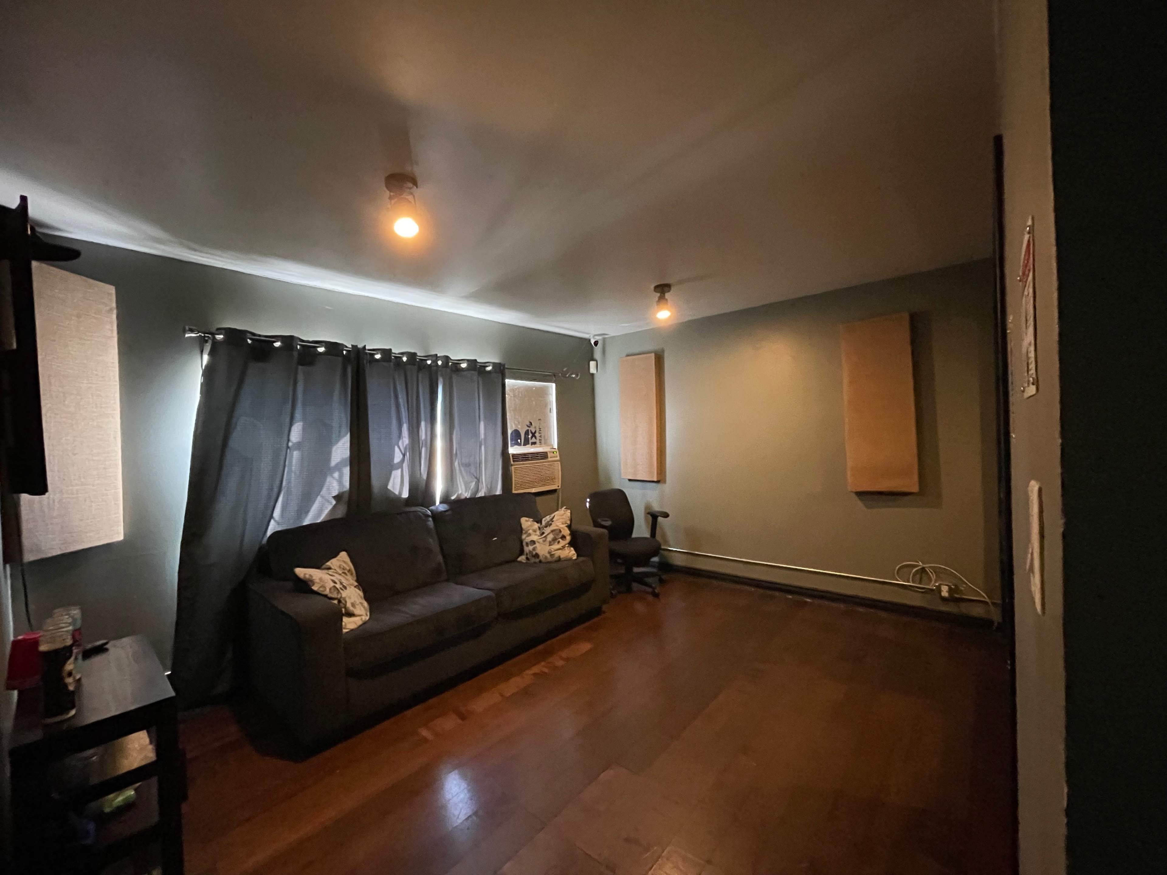 A living room with a dark sofa, curtains, an air conditioning unit, and wall-mounted acoustic panels.