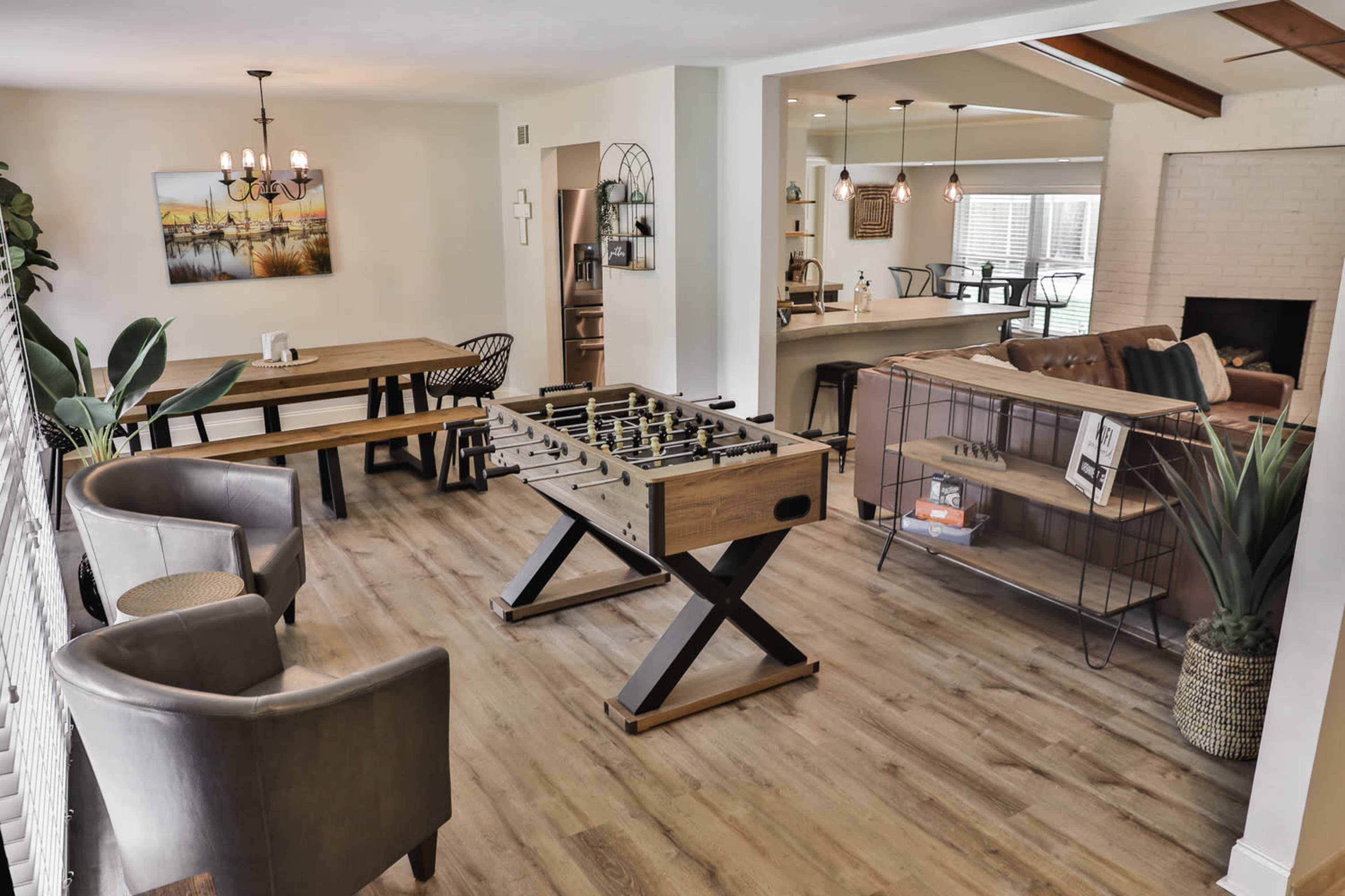 A spacious indoor area with a foosball table, a wooden dining table, two chairs, and a living room visible in the background.
